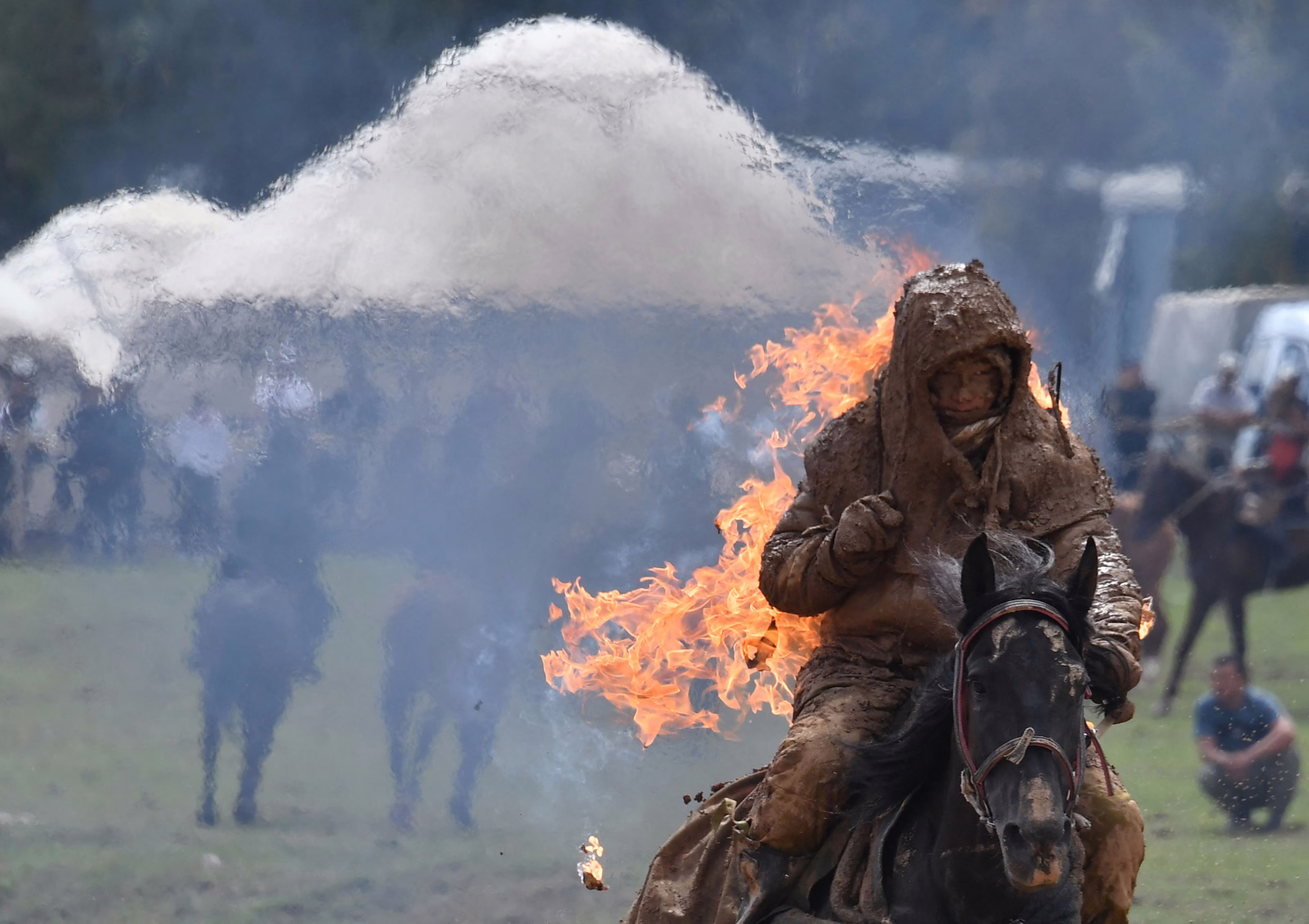 A rider on a horse, covered in mud and thick clothing, rides while on fire during a demonstration.