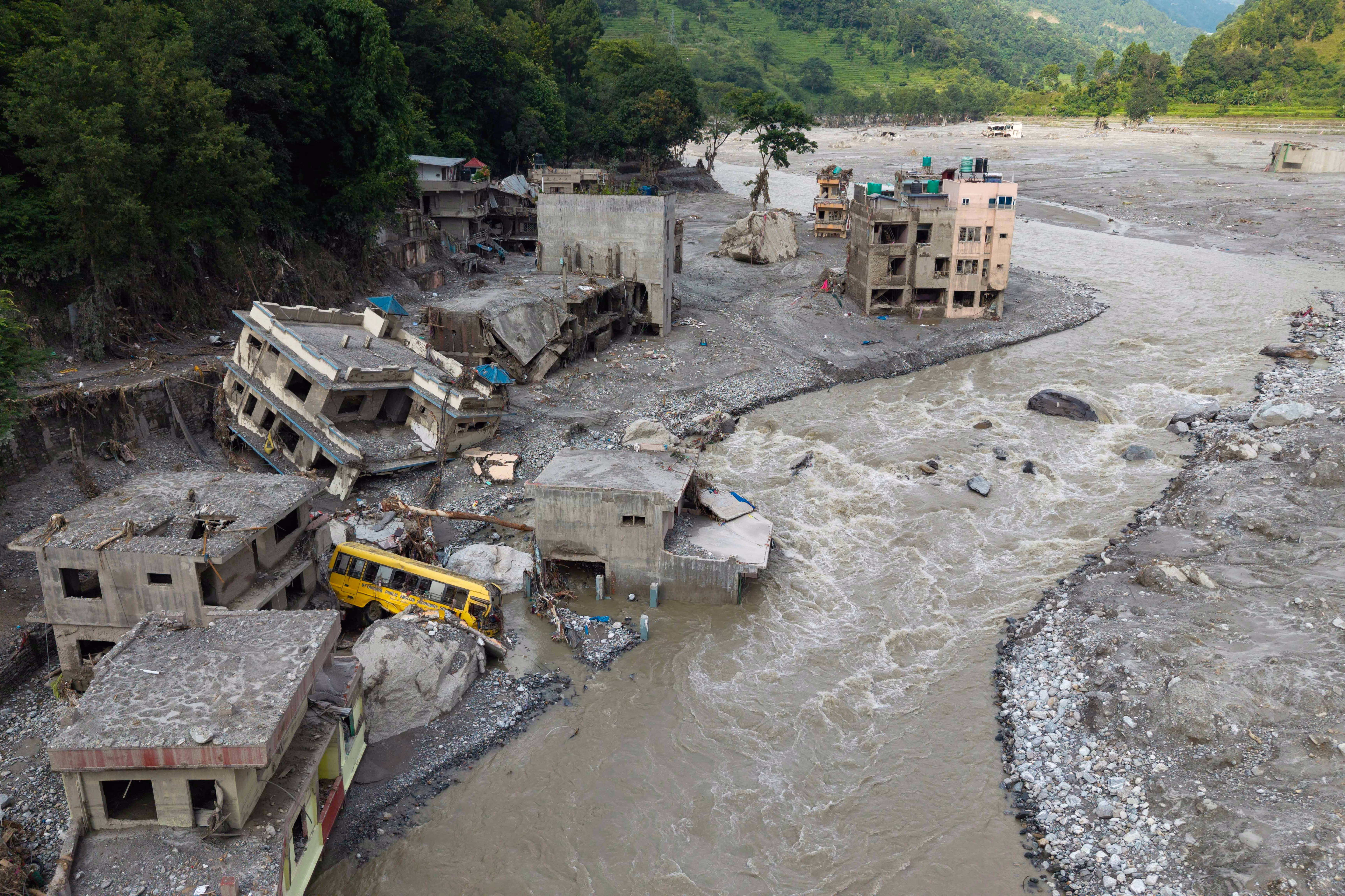 A muddy river rushes past badly-damaged houses and a scoured shoreline after a flash flood.