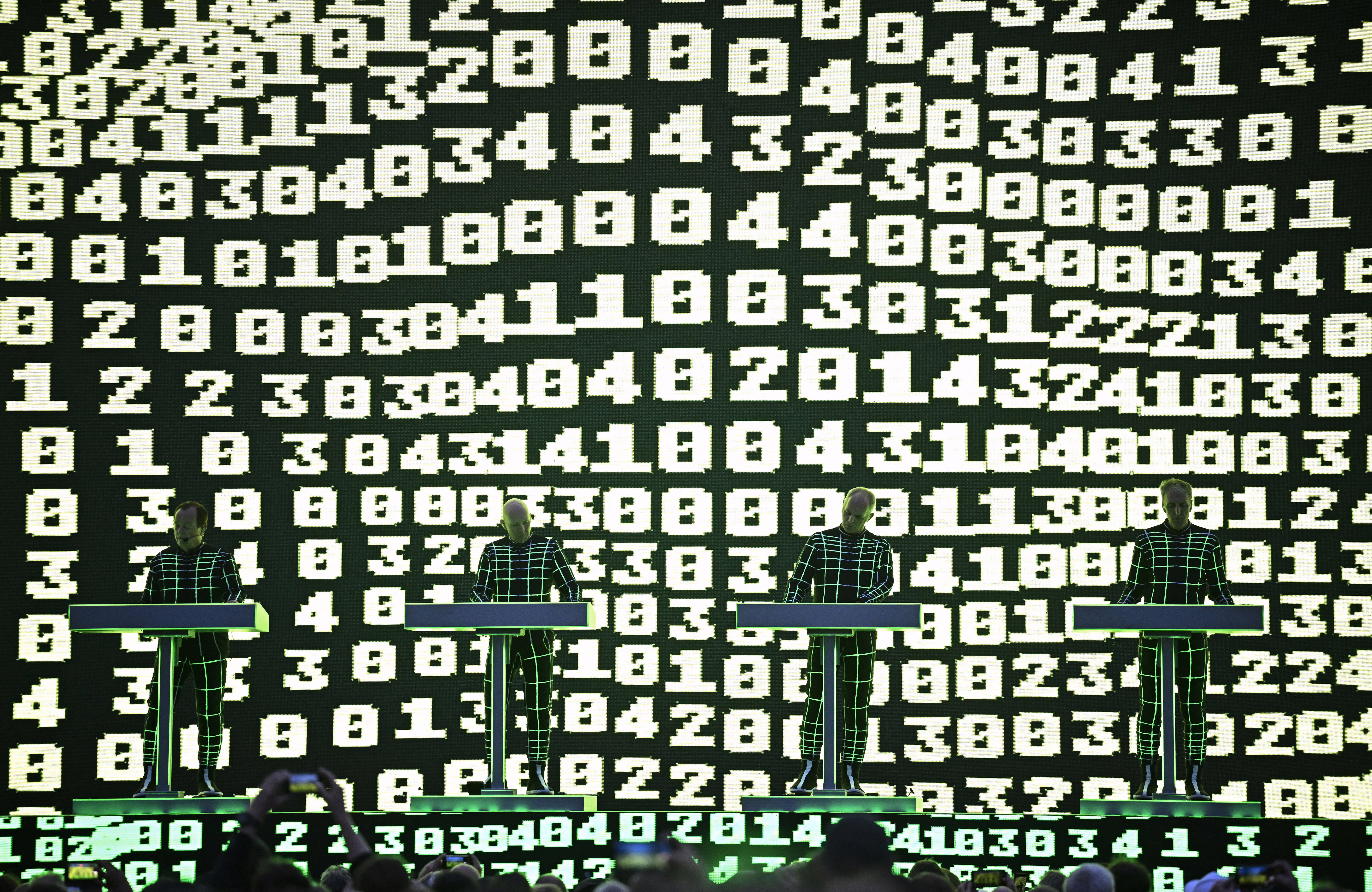 The German band Kraftwerk performs in front of a large video screen that is covered in dozens of blocky numbers.