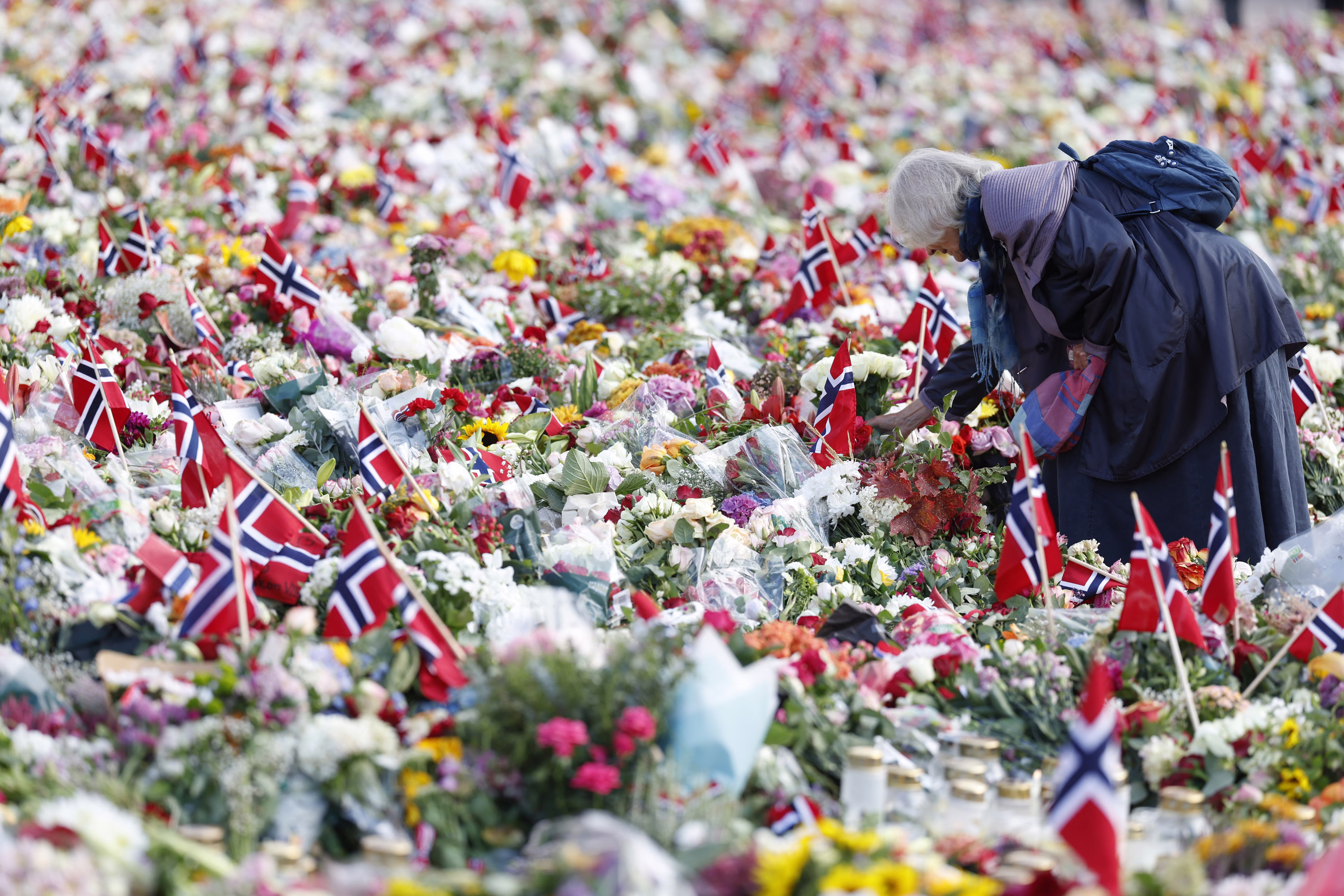 A woman places flowers at a makeshift memorial filled with thousands of bouquets and Norwegian flags.