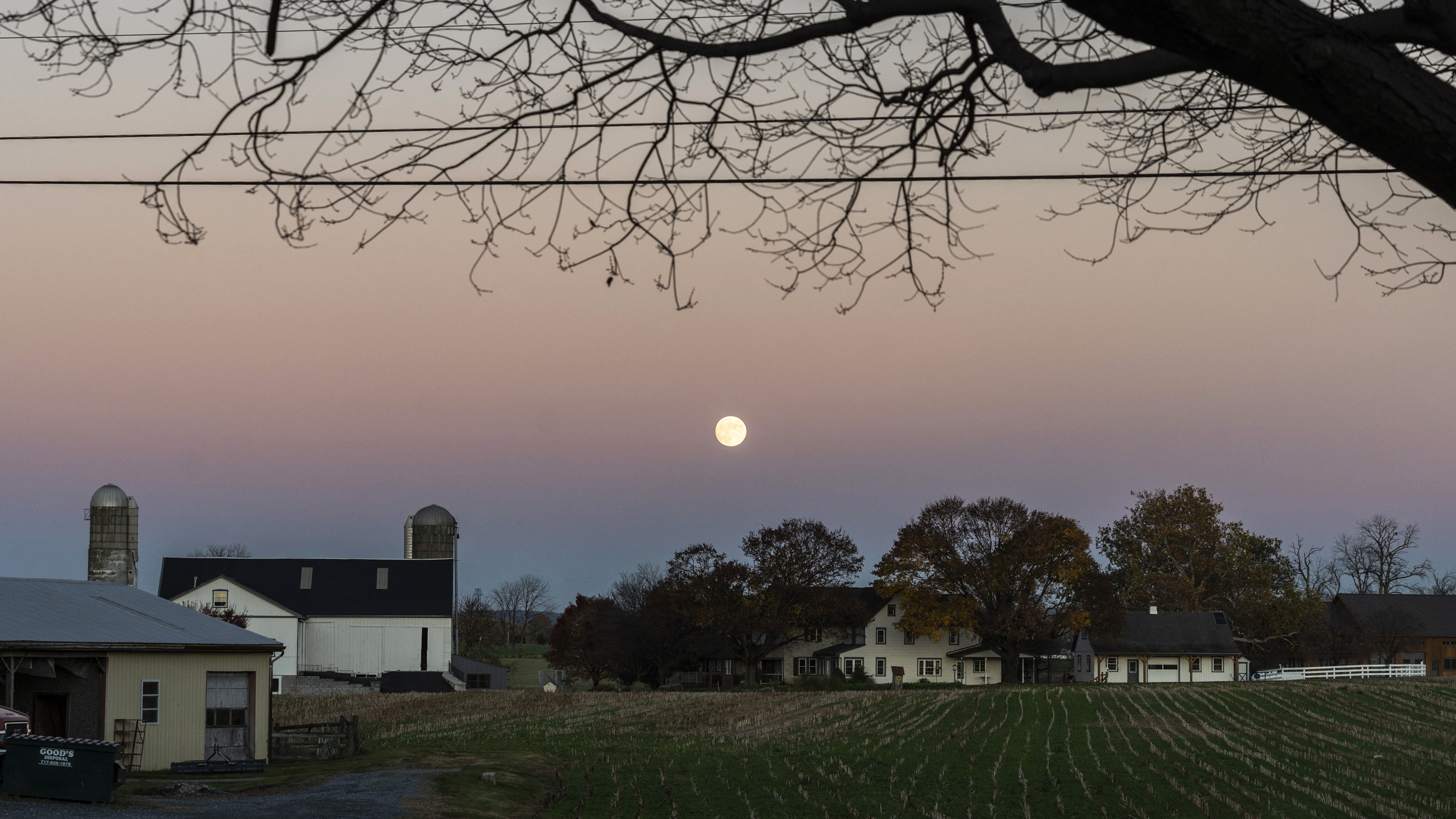 A full moon at dusk over green, sprawling farmland
