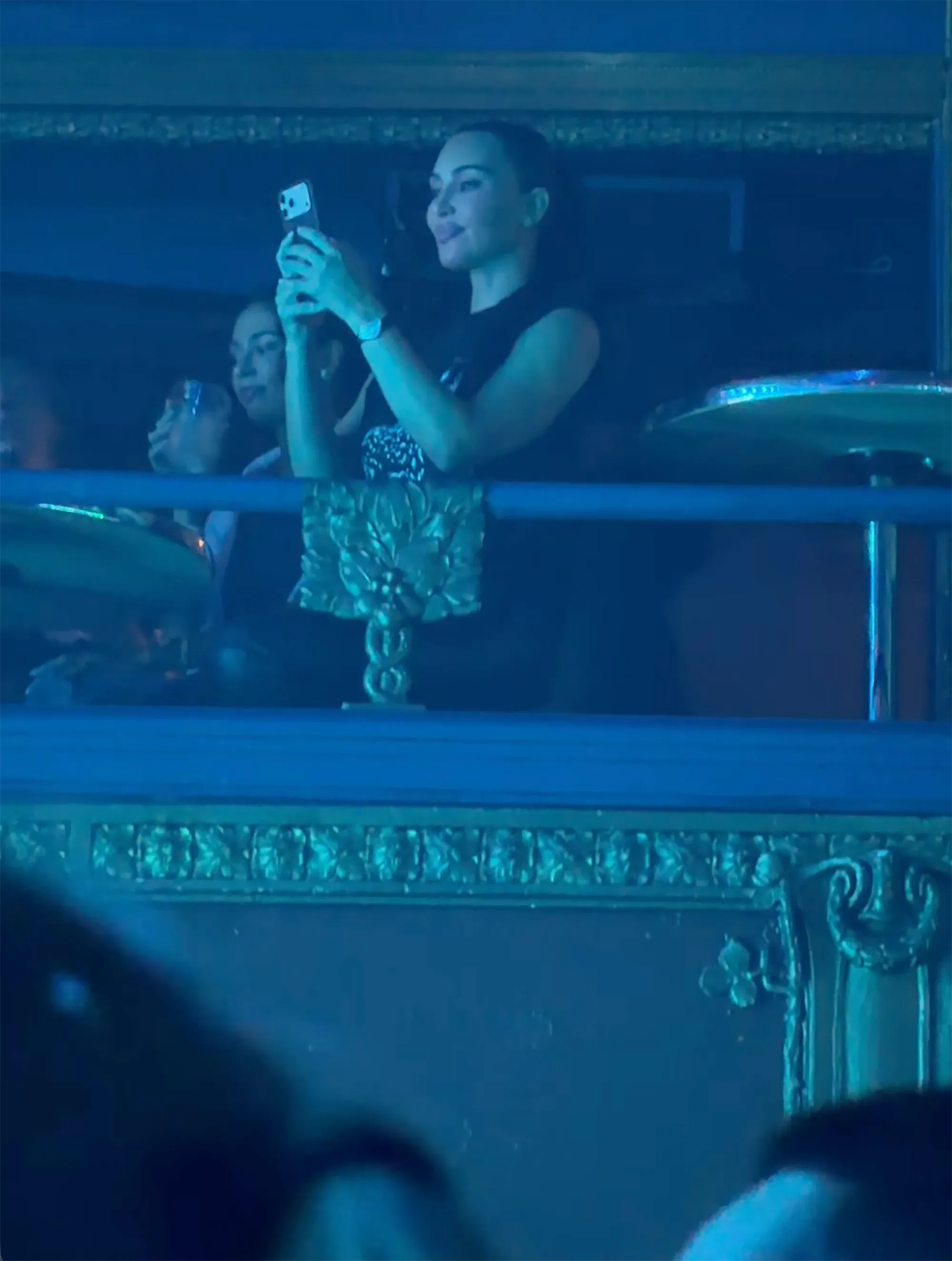 Kim Kardashian taking a photo with her phone from a balcony at her daughter North's solo concert.