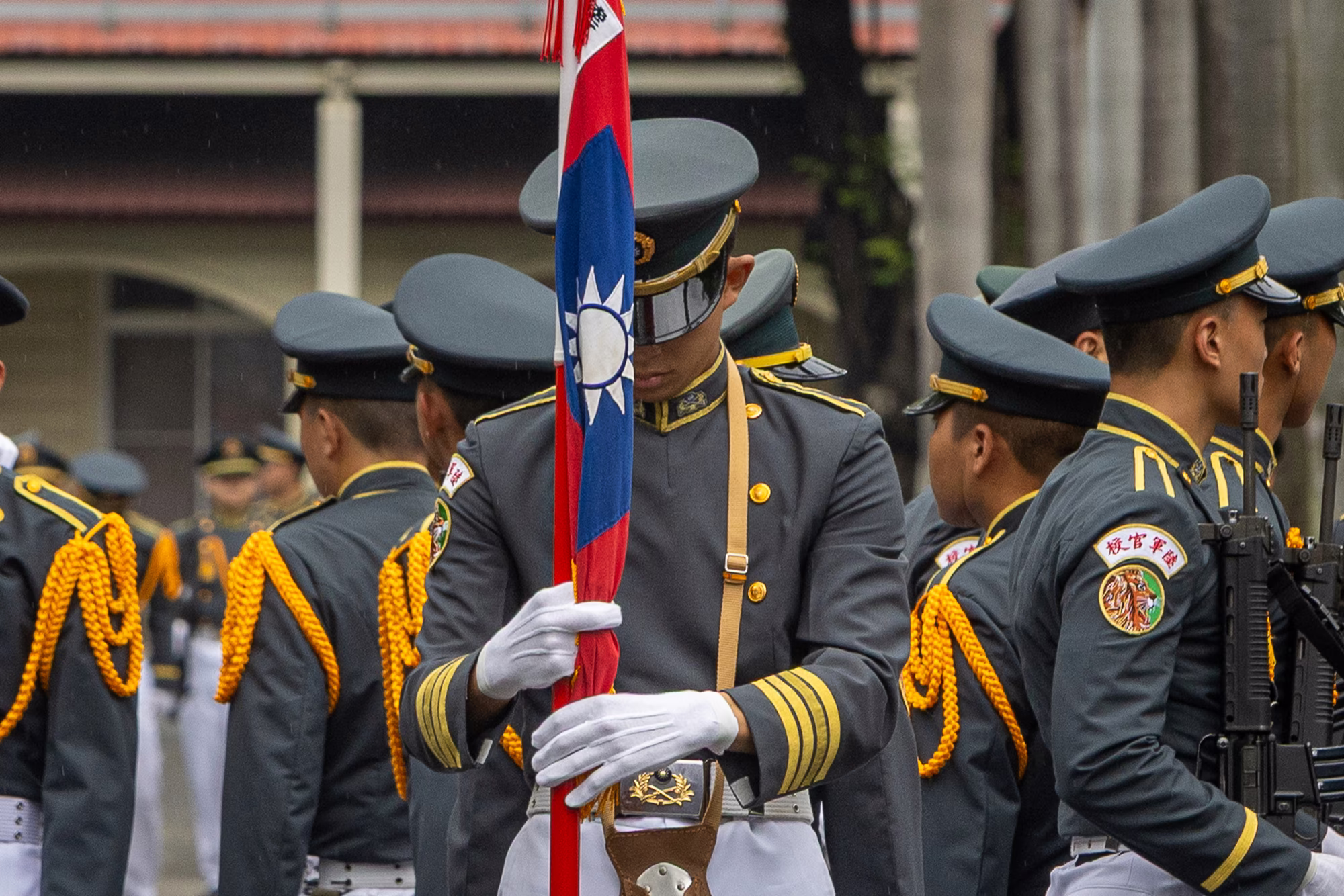 photo of male cadet in dress uniform gathering flag in hand, surrounded by other cadets, some armed.
