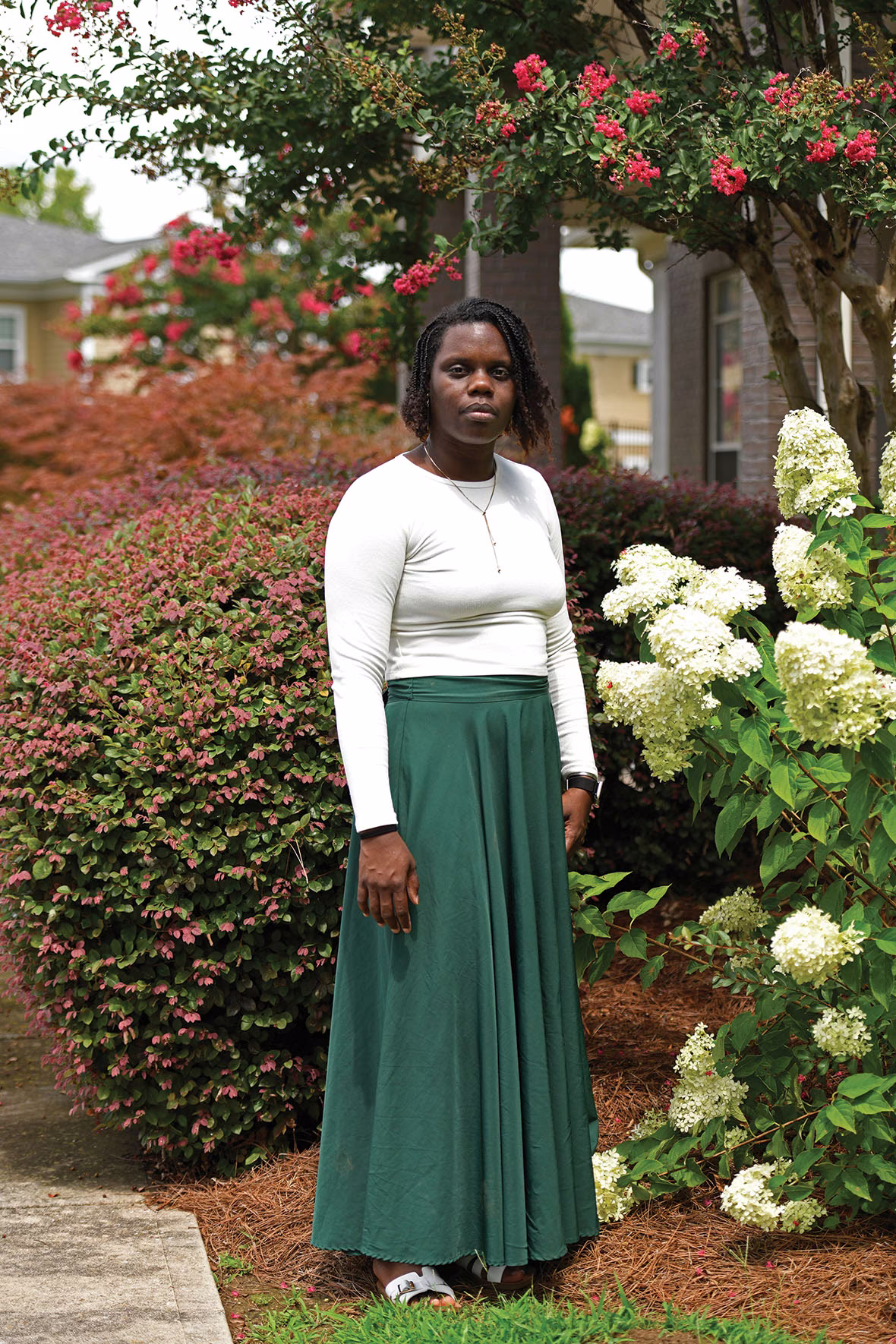 photo of woman wearing white long-sleeved shirt and long green skirt outside with flowers and trees in background