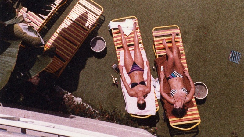 Two women in bikinis splayed out on plastic lounge chairs.