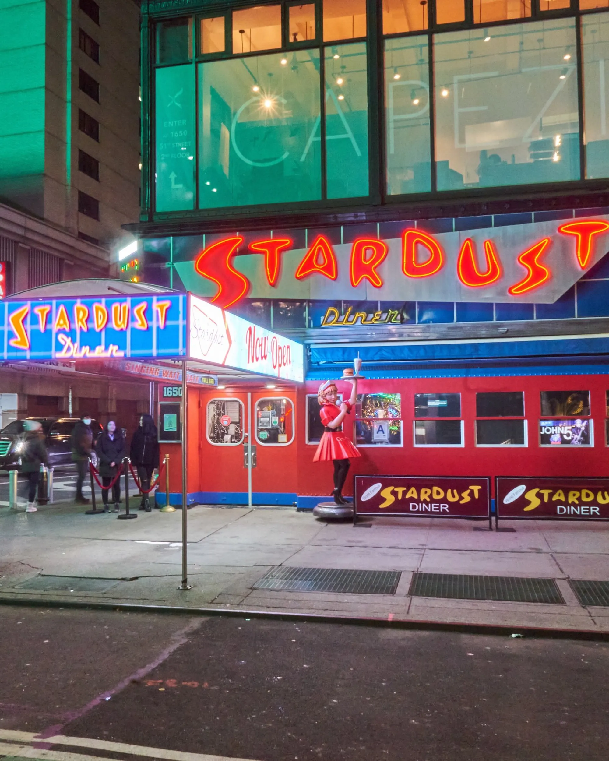 The exterior of Ellen's Stardust Diner in New York City with bright neon signs and a statue of a waitress holding a tray.