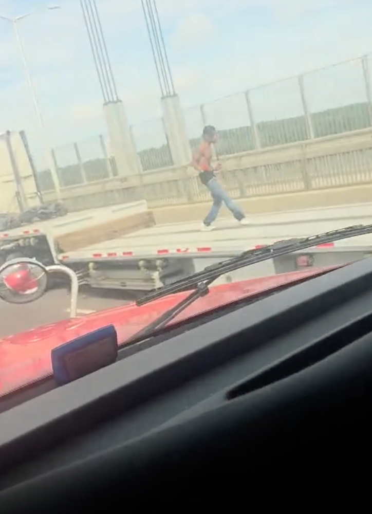 A shirtless man running on a highway bridge.