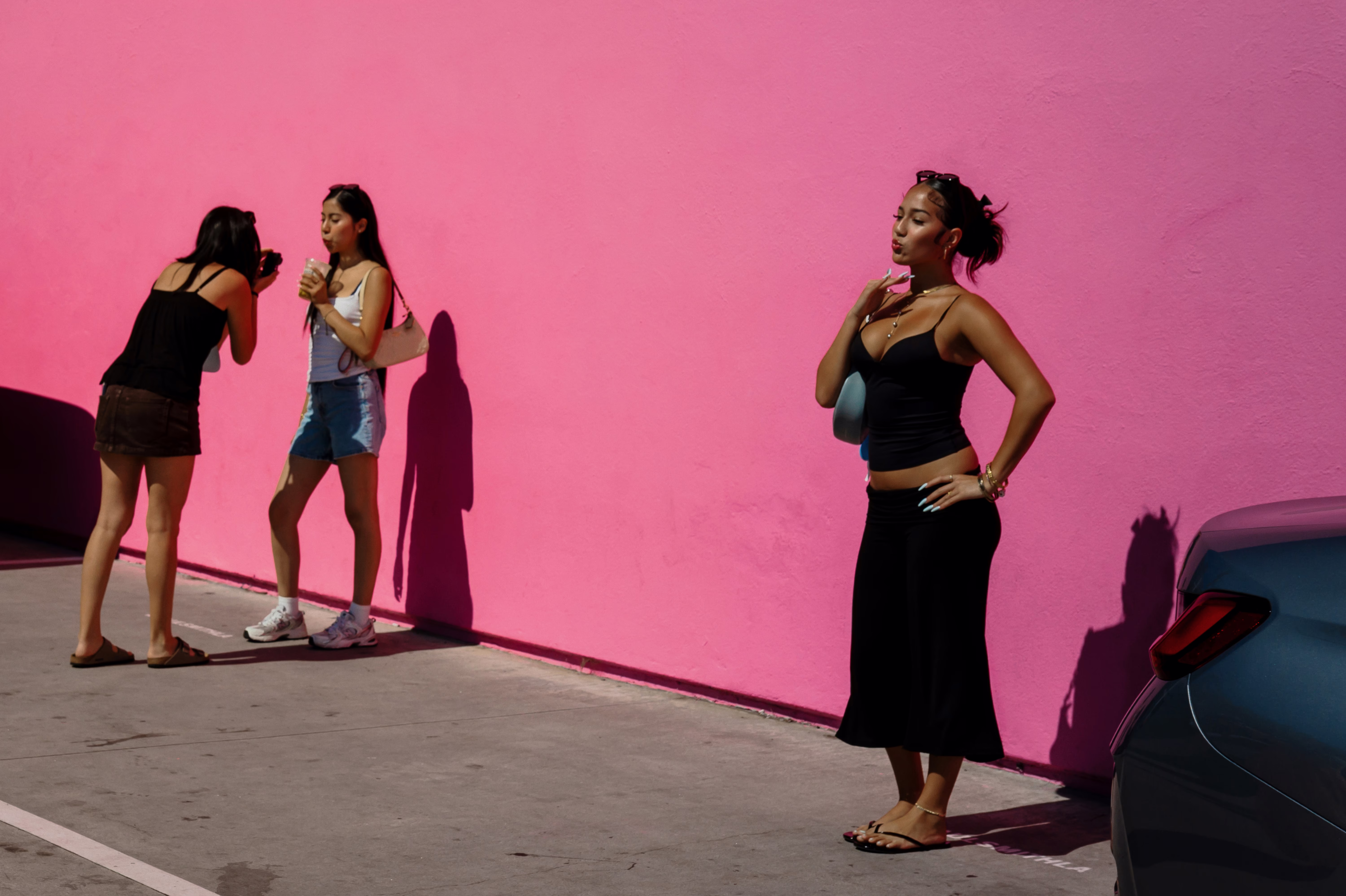 photo of women taking photos and selfies outdoors against a bright pink wall 