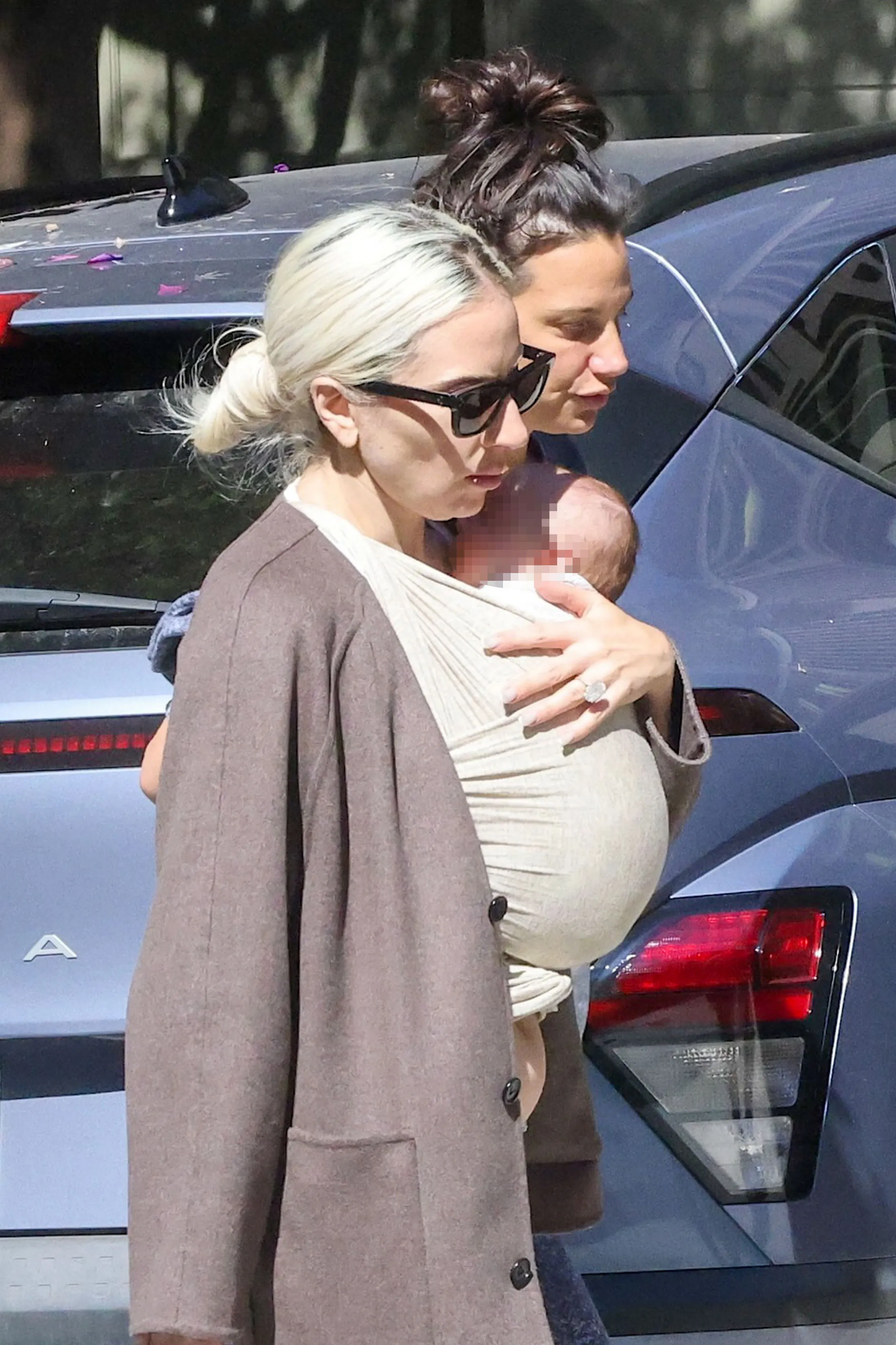 Lady Gaga carrying a baby in a wrap with Michael Polansky walking behind her.