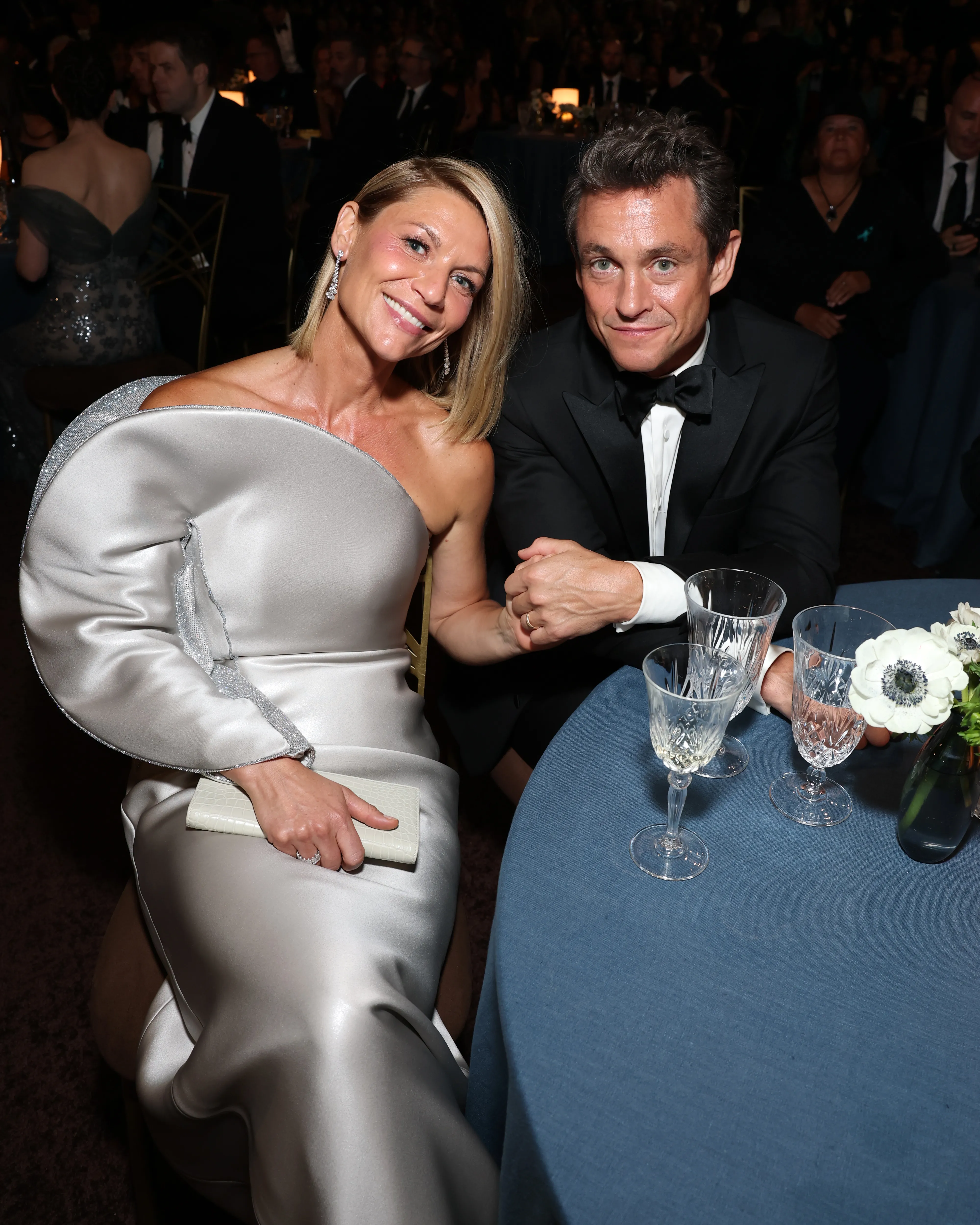 Claire Danes and Hugh Dancy sitting at a table with drinks and flowers.