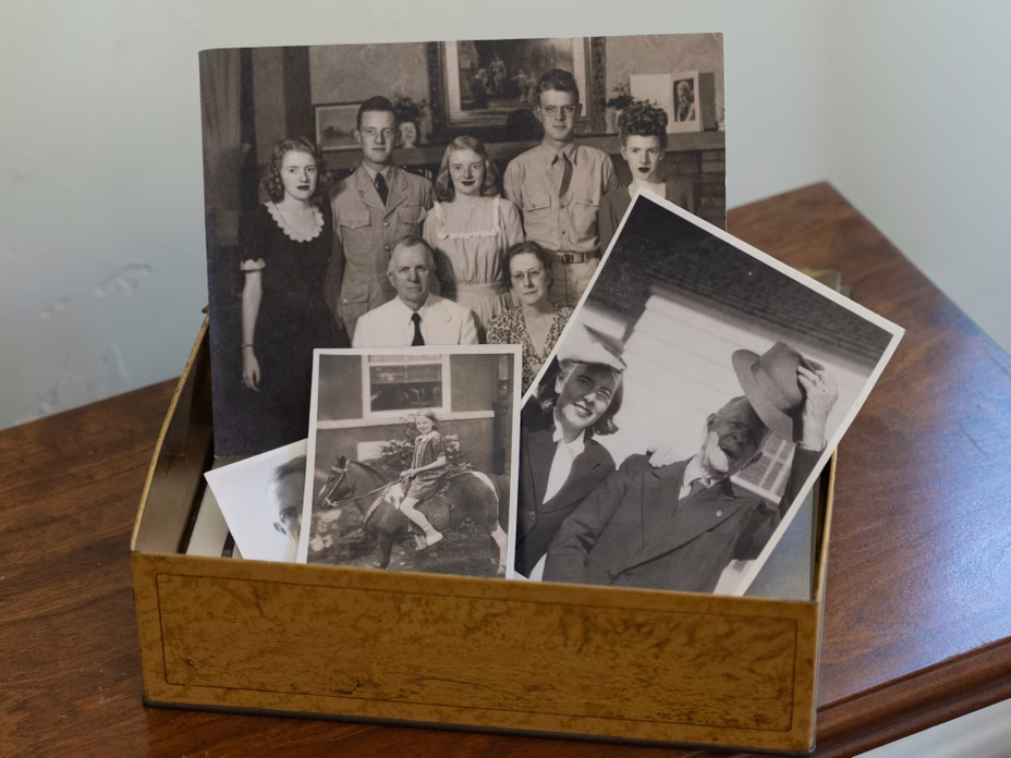 photo of a box of archival black-and-white family photos including a group family shot, a girl on a pony, and a woman standing next to a man in a fedora