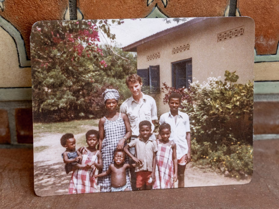 photo of candid color snapshot of tall man standing with woman and half a dozen children in front of building with doors open and flowering trees