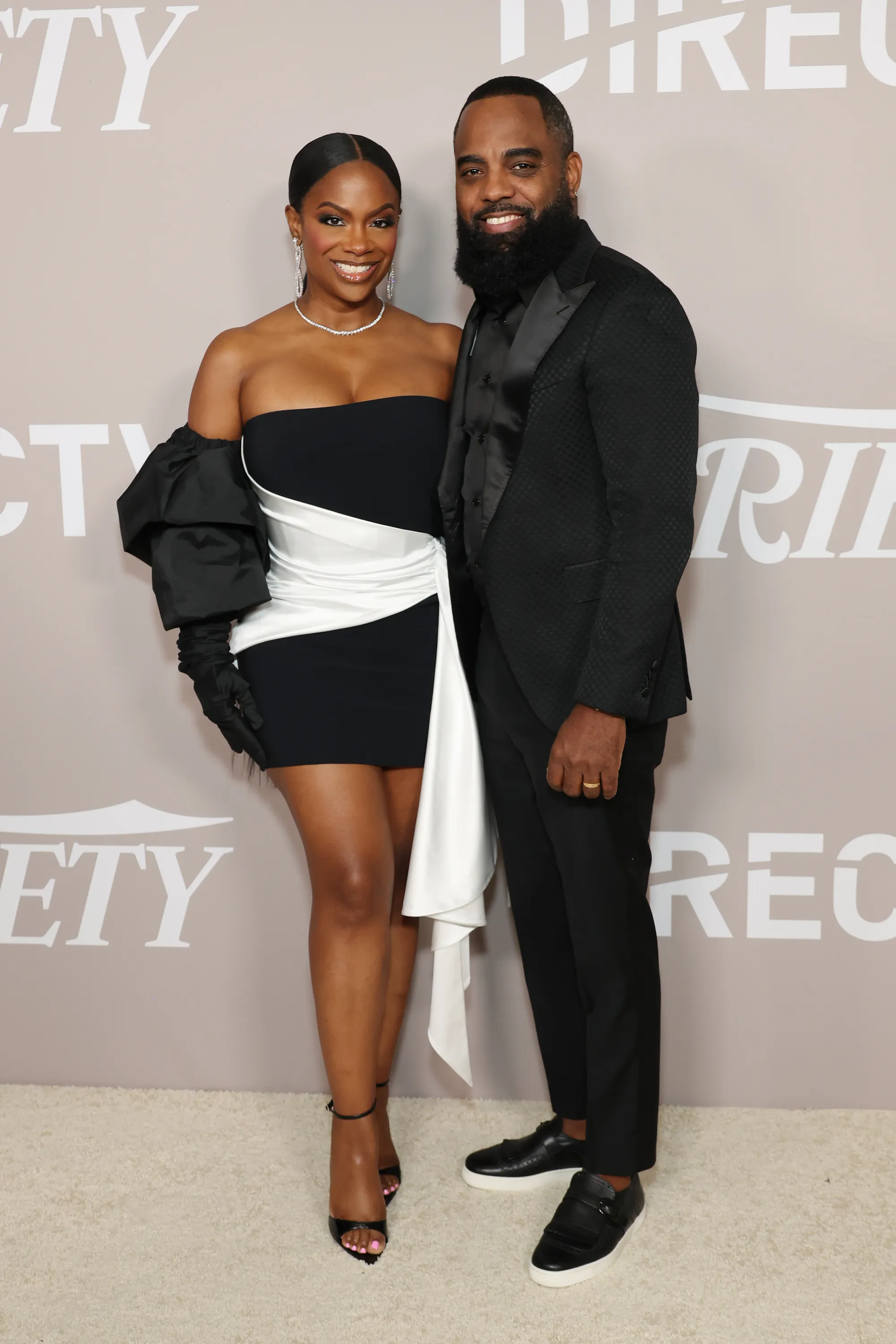 Kandi Burruss in a black and white dress and Todd Tucker in a black suit pose for a photo.
