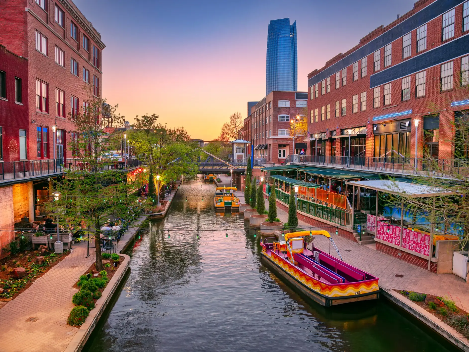 Bricktown Canal in Oklahoma City winds between red brick buildings and water taxis at sunset.