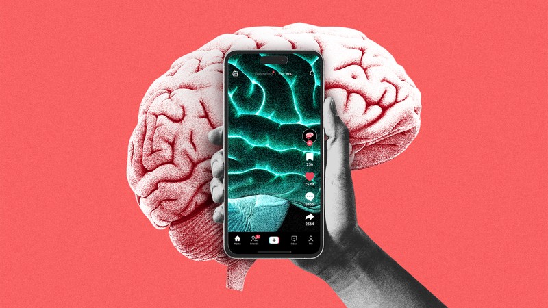 A human brain being obscured by a hand holding a phone playing a short-form video app, which shows a green, glowing human brain