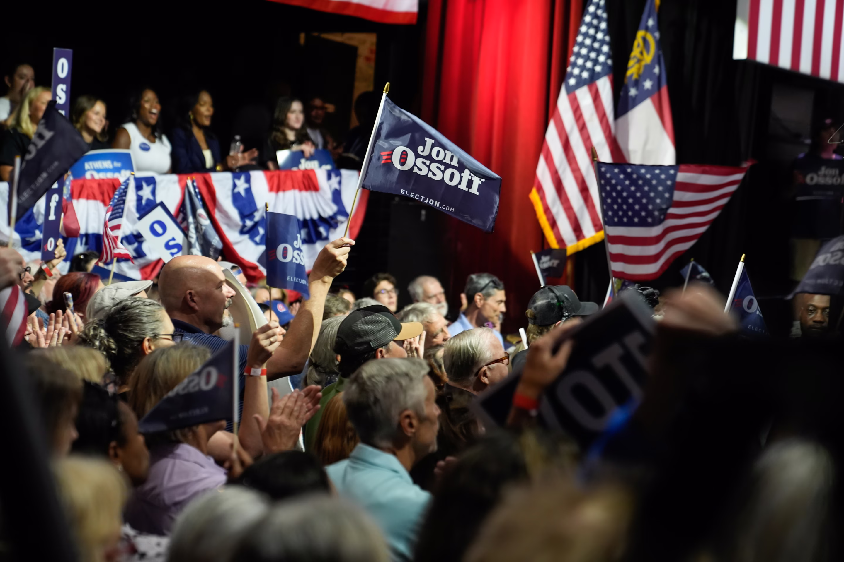 a person holds a Jon Ossoff flag in a crowd