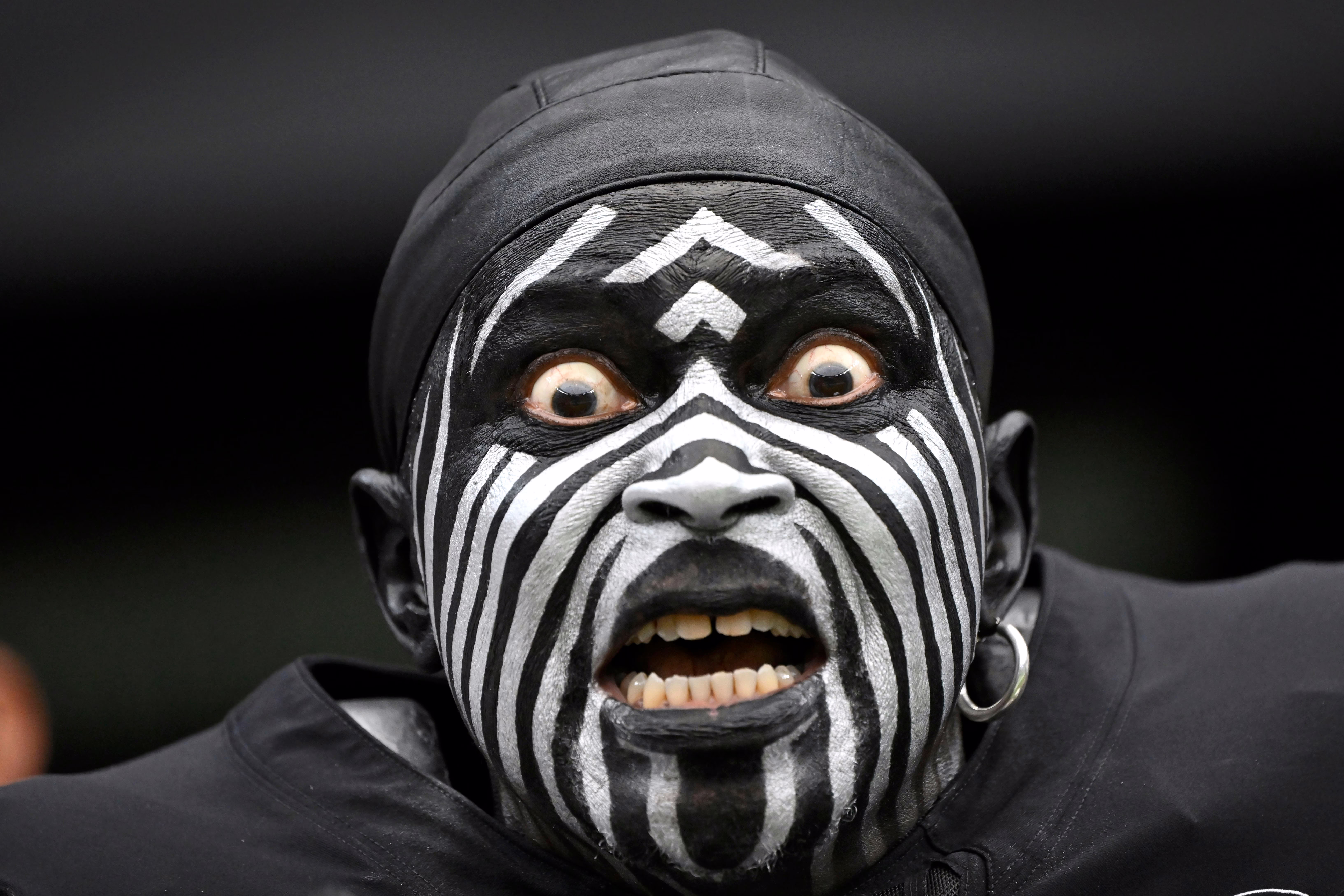 A fan reacts before a football game, their face painted black with white stripes.