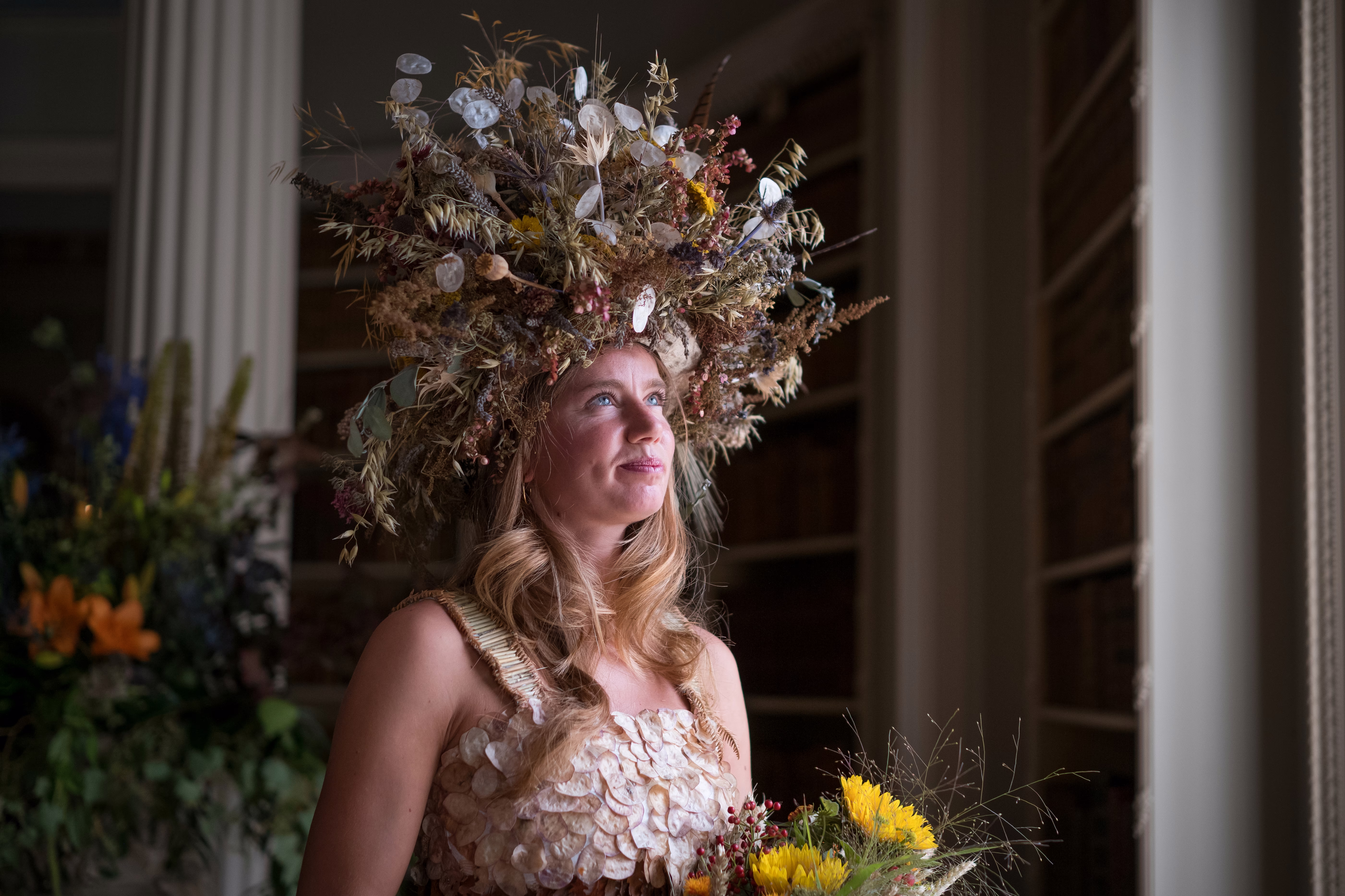 A model poses, wearing a dress and headgear adorned with autumnal foliage.