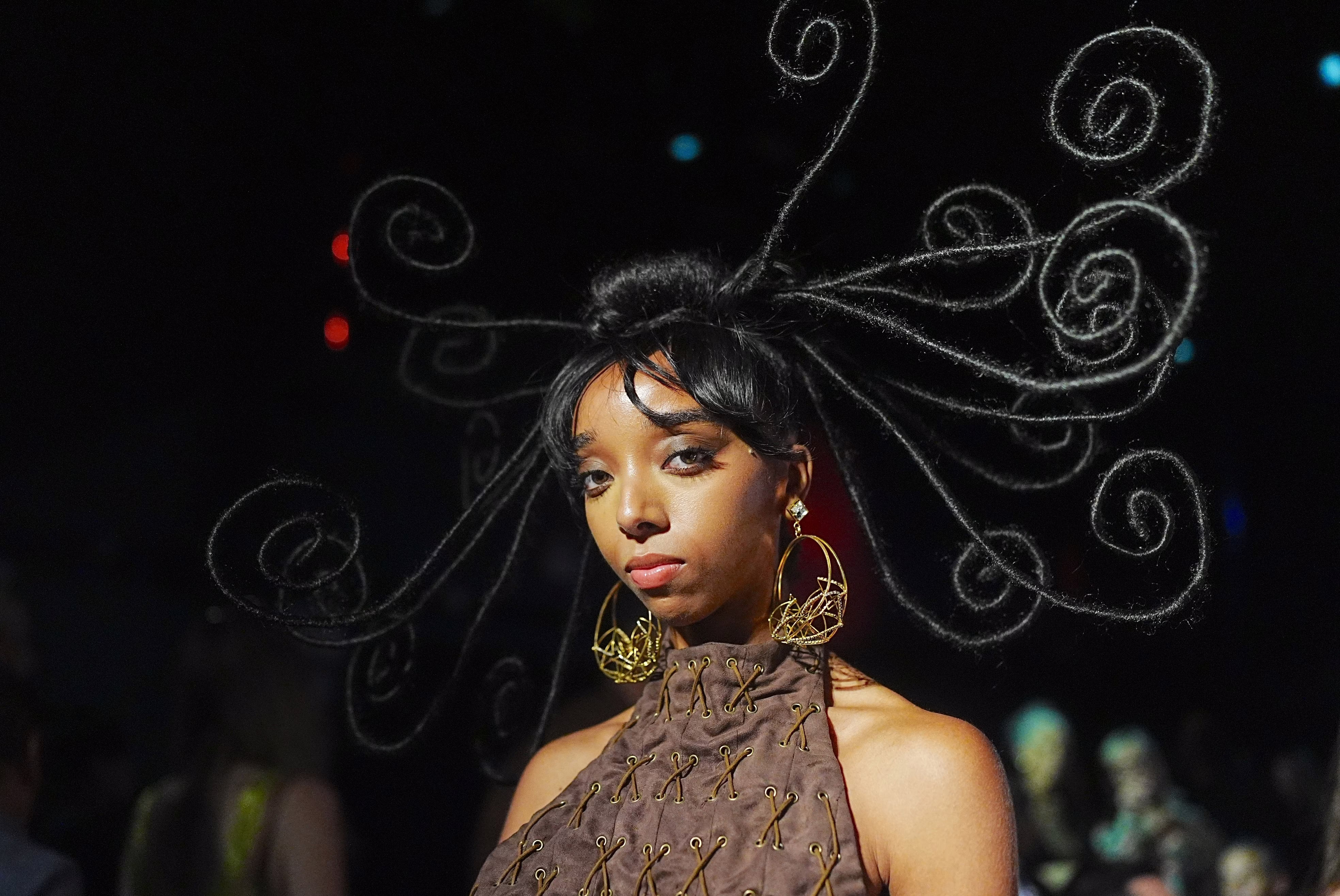 An artist with long and curling hair extensions poses at a fashion show.