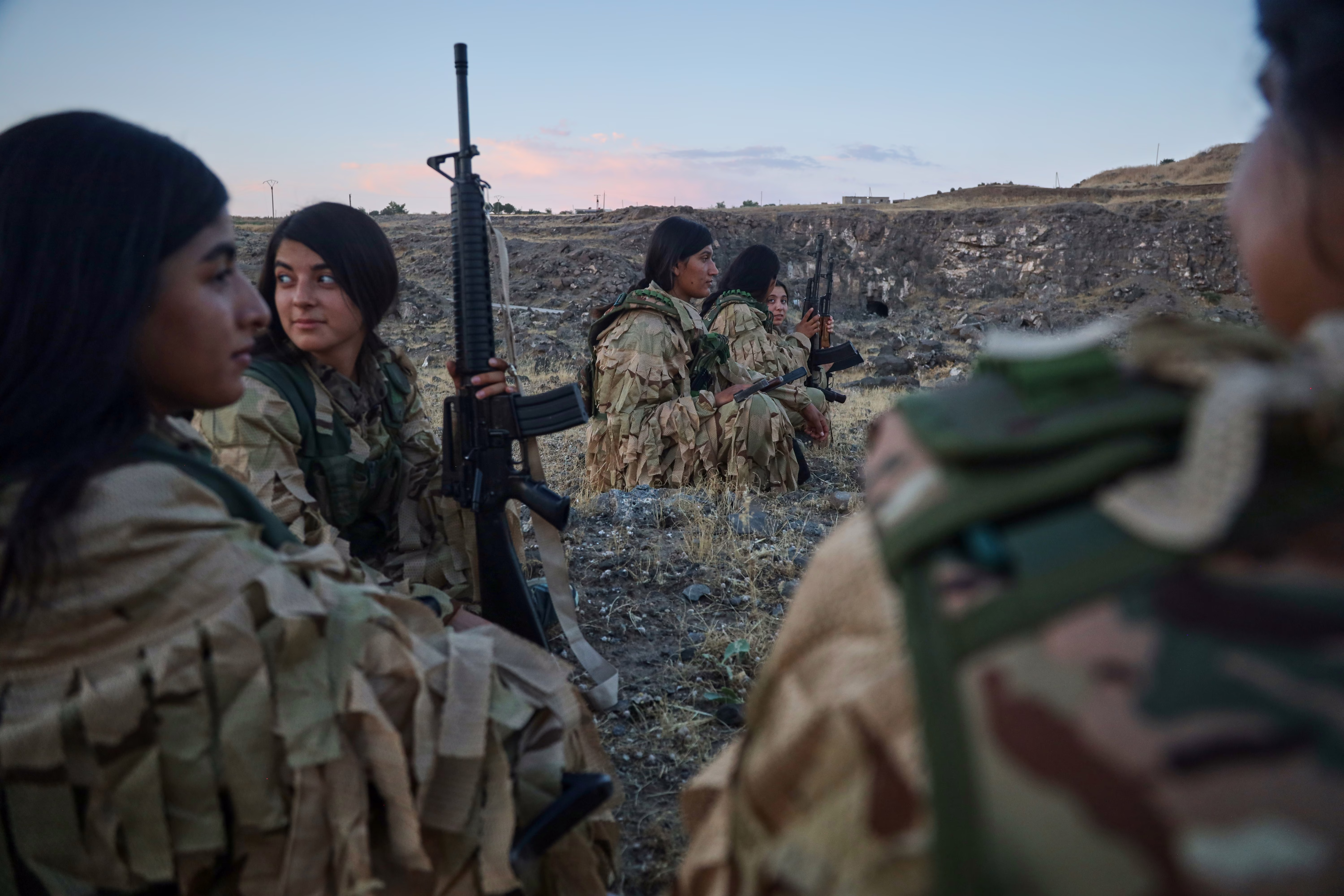 A half-dozen female soldiers rest in an open area during a training session.