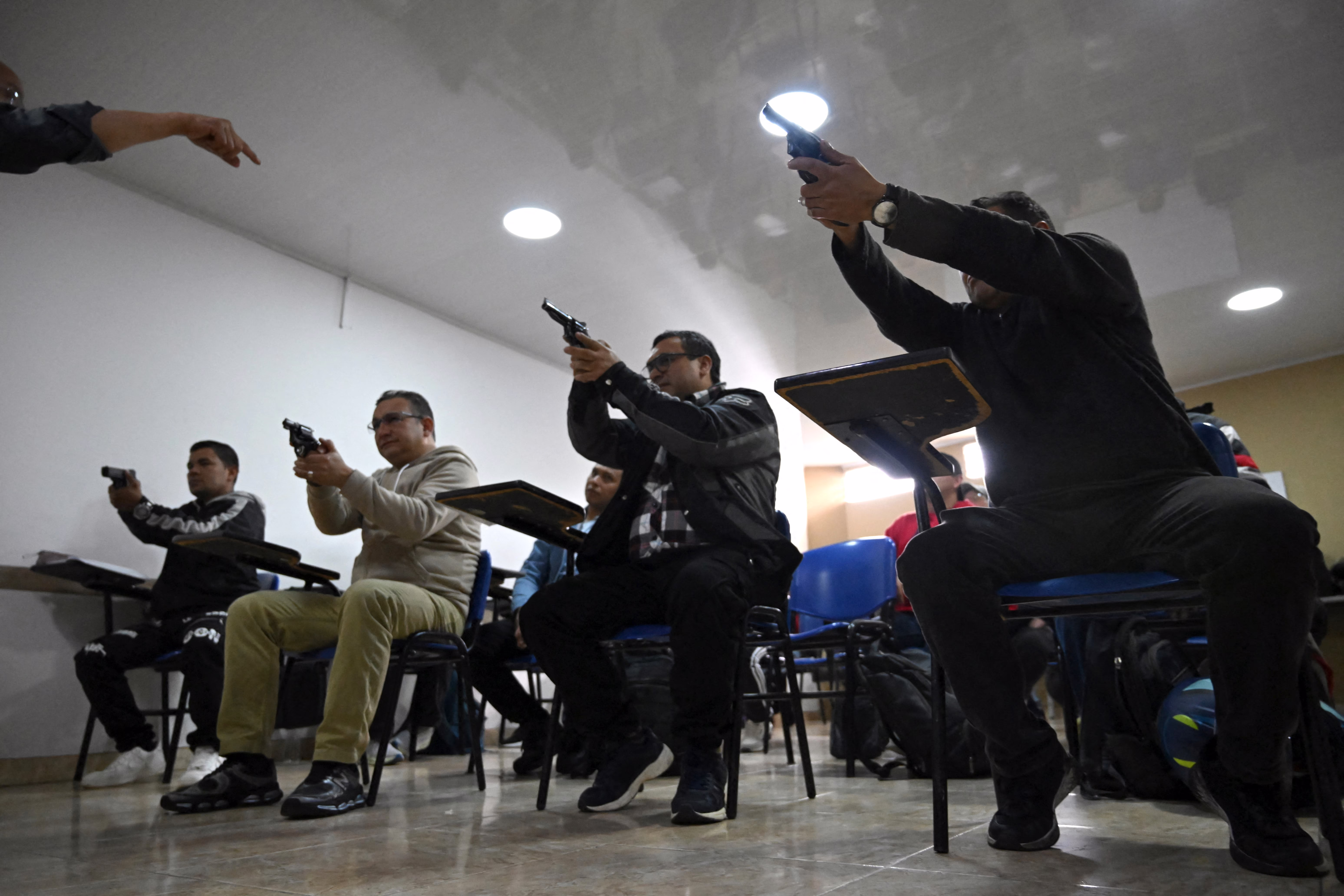 People seated in classroom seats hold up pistols during a weapons-training session.