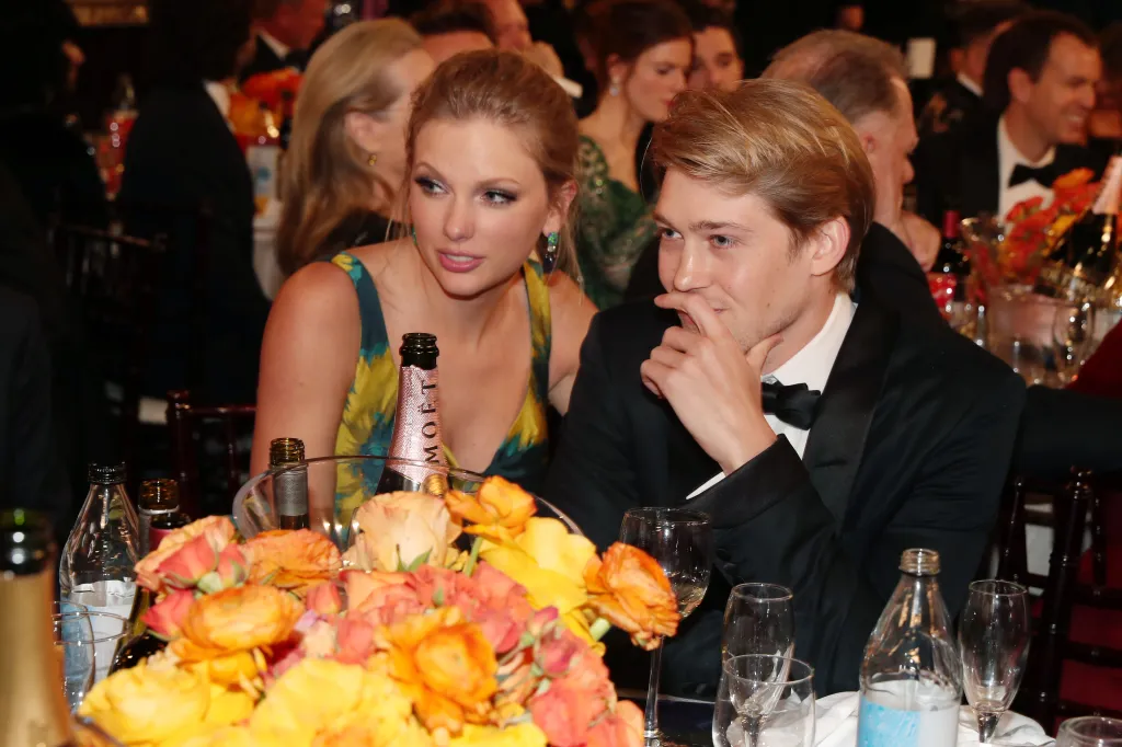 Taylor Swift in a green and yellow dress sits with Joe Alwyn in a black tuxedo at the Golden Globe Awards.