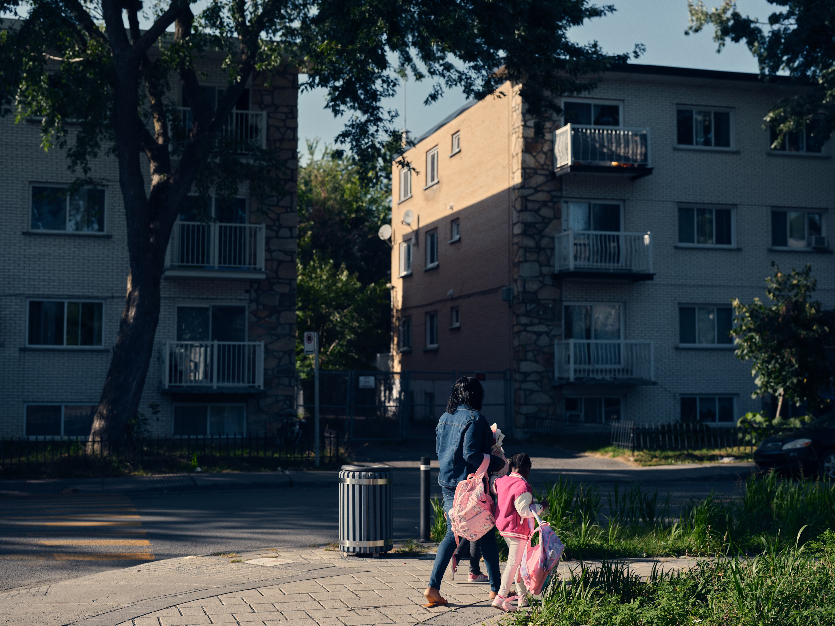 a woman and girl walk in front of apartment buildings