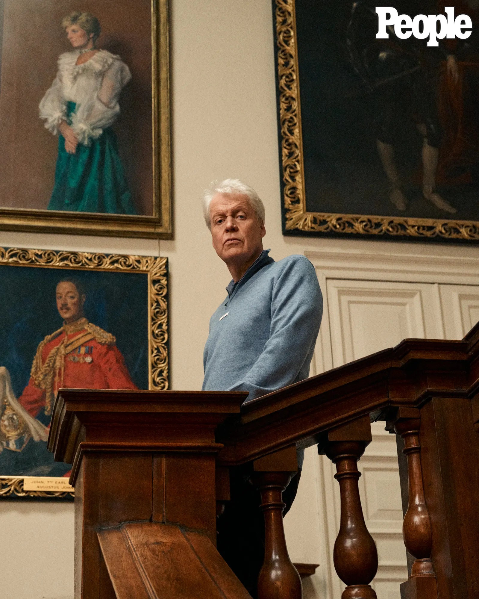 Charles Spencer stands on a wooden staircase with a portrait of Princess Diana hanging behind him.