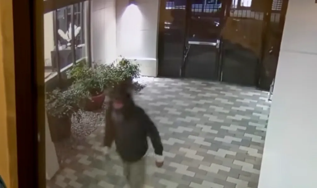 Surveillance footage of a man in a hooded sweatshirt walking through an outdoor patio area at night.