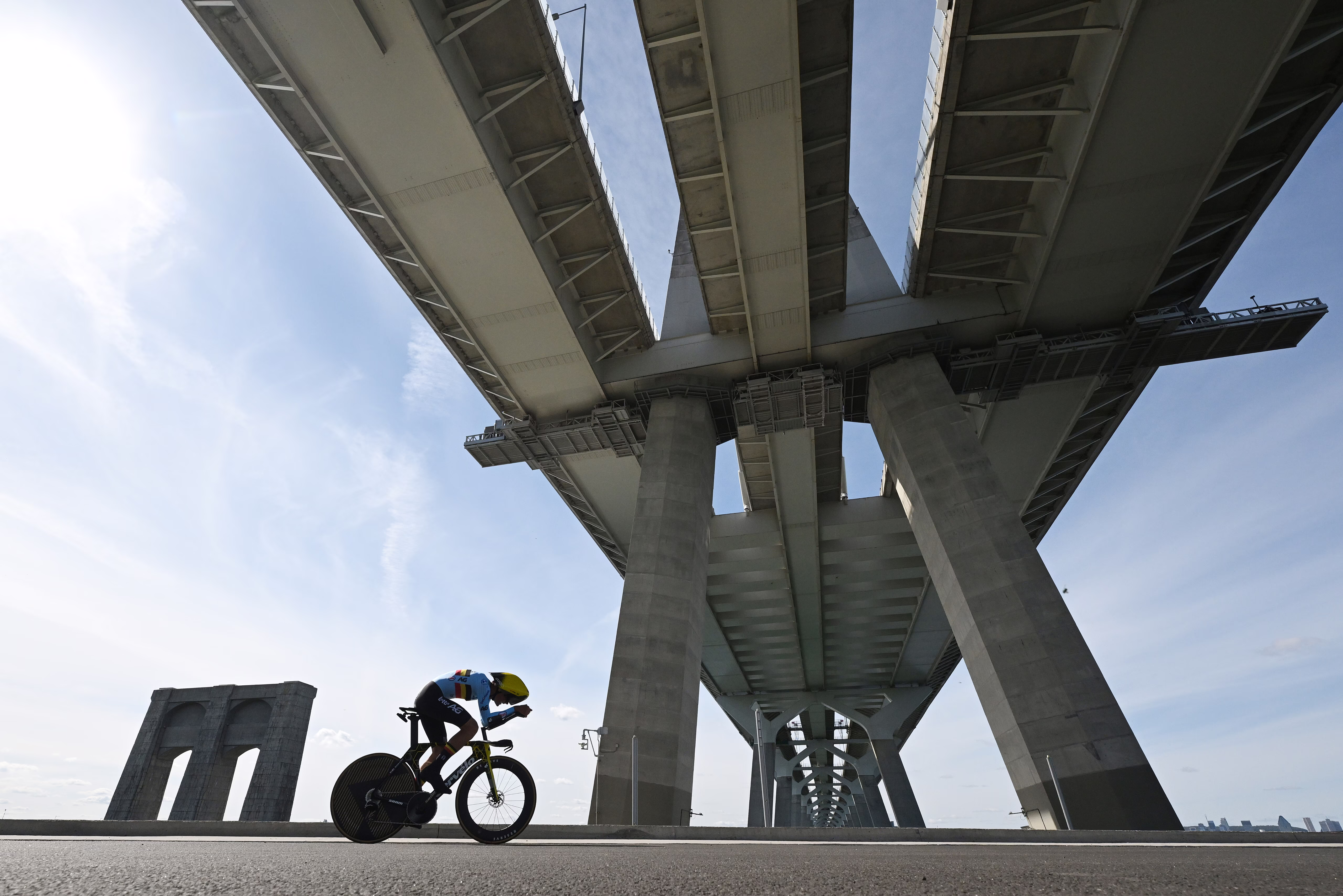 A cyclist rides during a time-trial race beneath a tall road bridge.