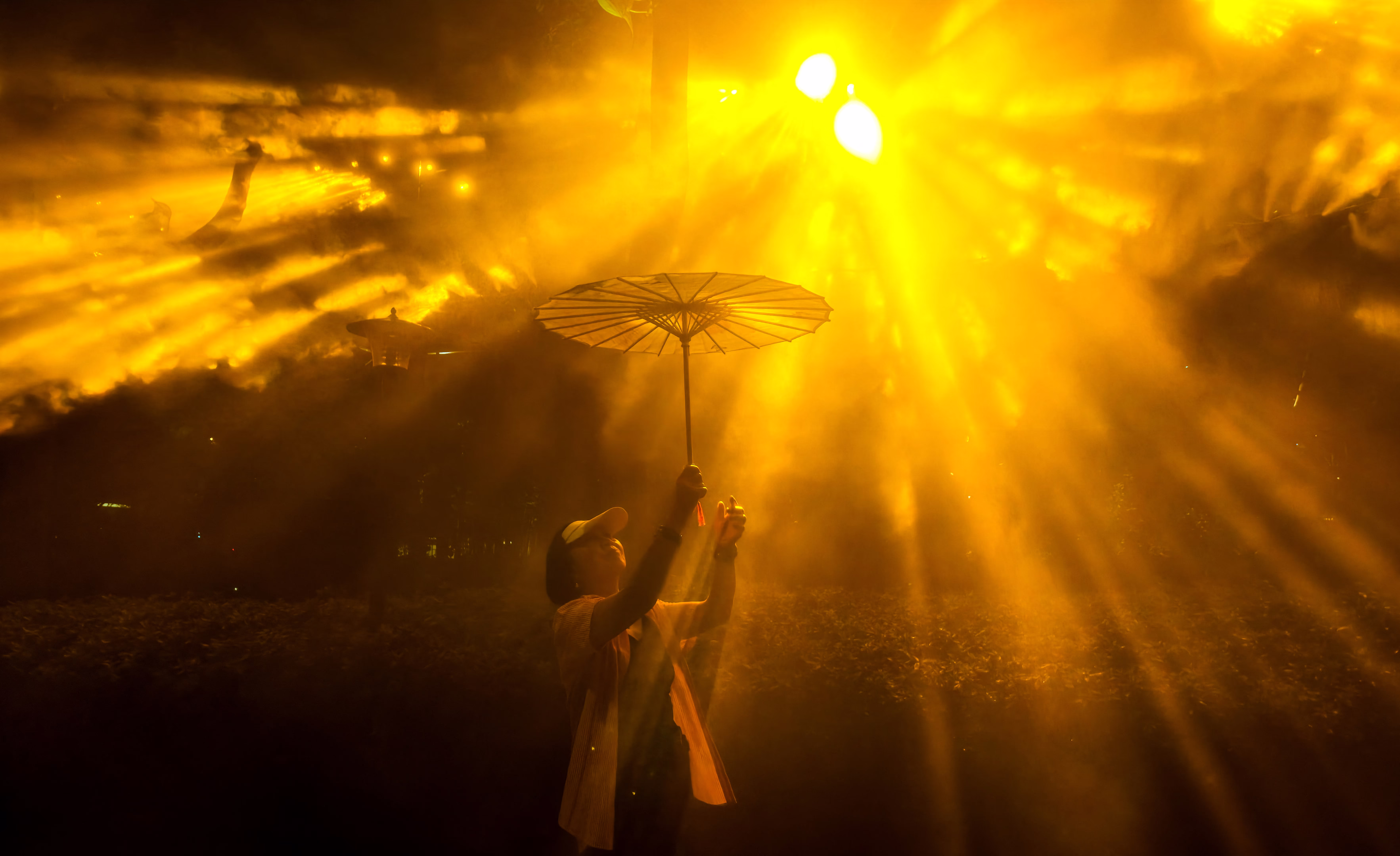 A woman holding an umbrella poses beside a light display.