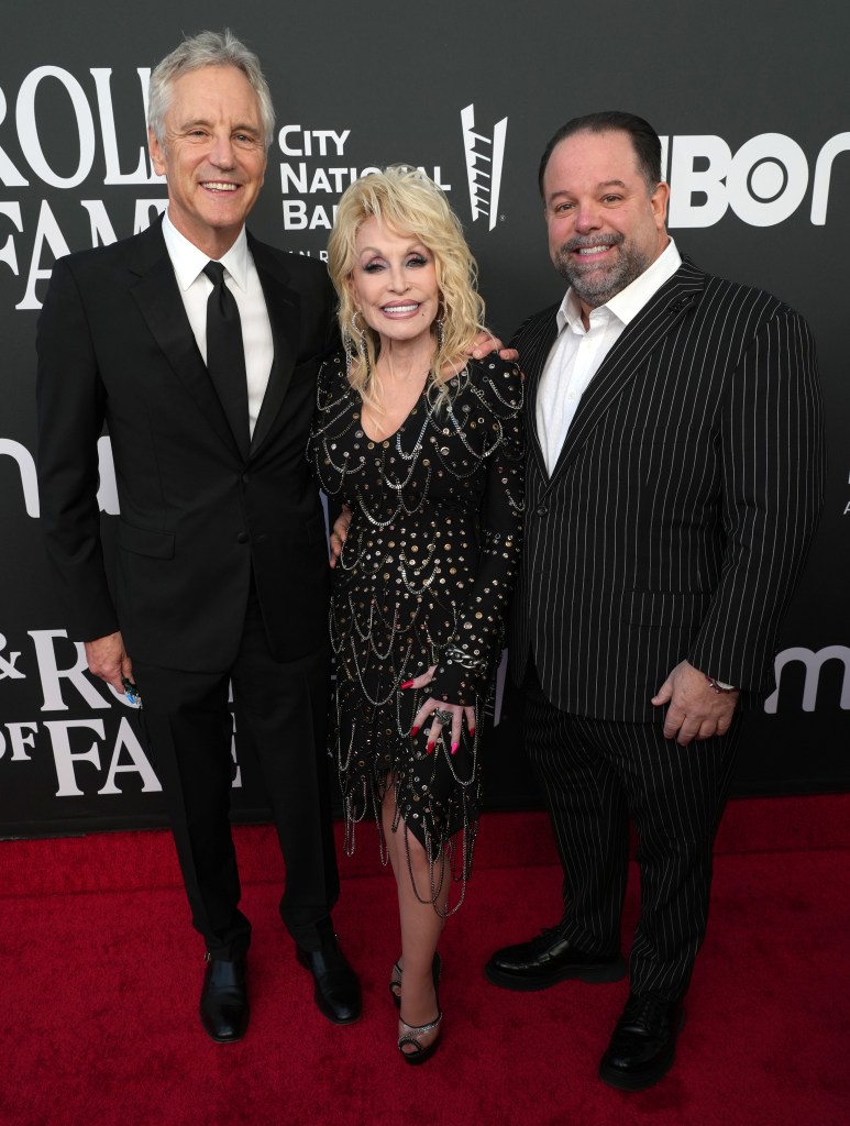 John Sykes, Dolly Parton, and Danny Nozell pose on the red carpet at the 37th Annual Rock & Roll Hall of Fame Induction Ceremony.