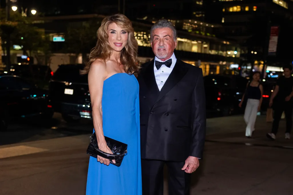 Jennifer Flavin in a blue dress and Sylvester Stallone in a black tuxedo stand side-by-side.