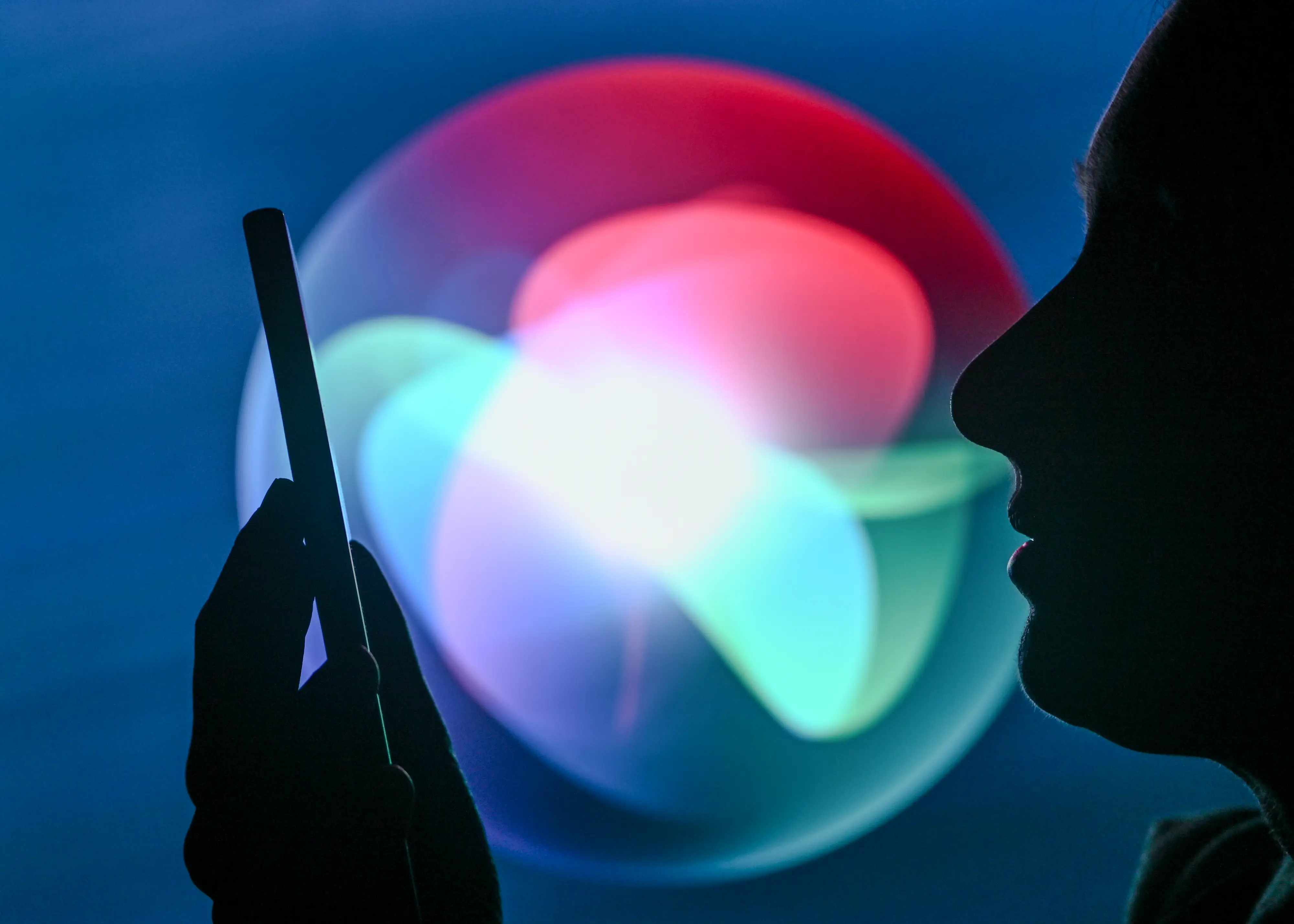 A dark silhouette of a person holding an iPhone in front of a Siri emblem.
