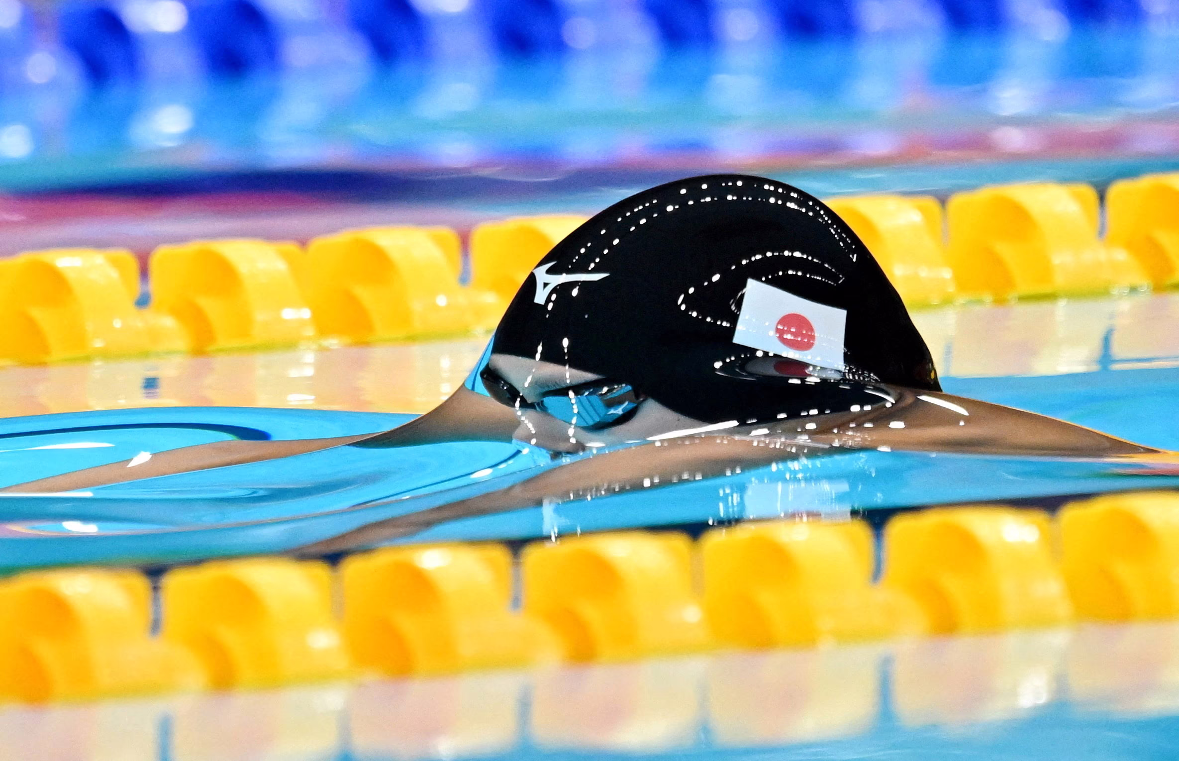 A swimmer reaches the surface of a pool during a race, the water smoothly clinging to them, giving a distorted view of their head.