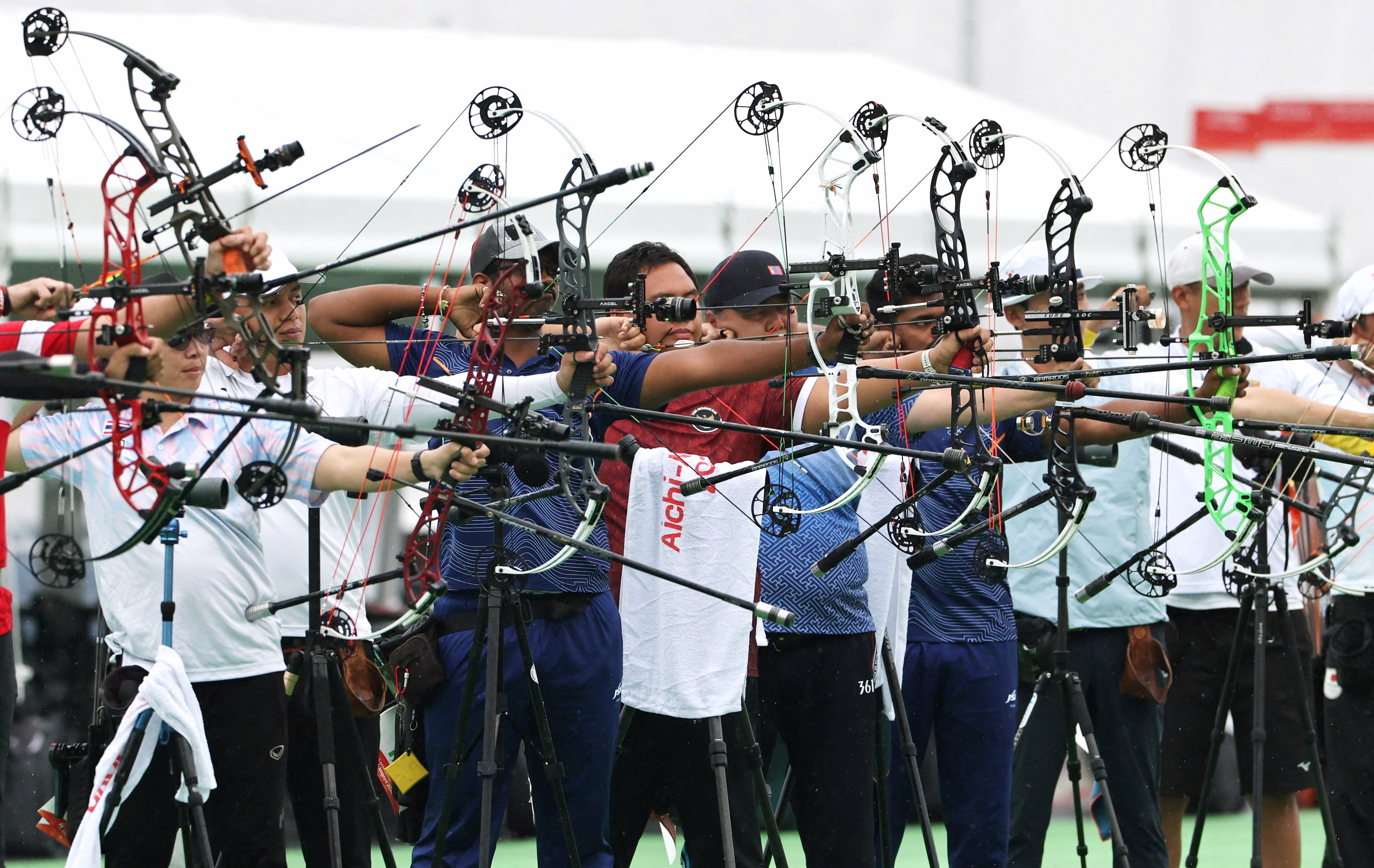 Many archers stand side-by-side, aiming their compound bows.