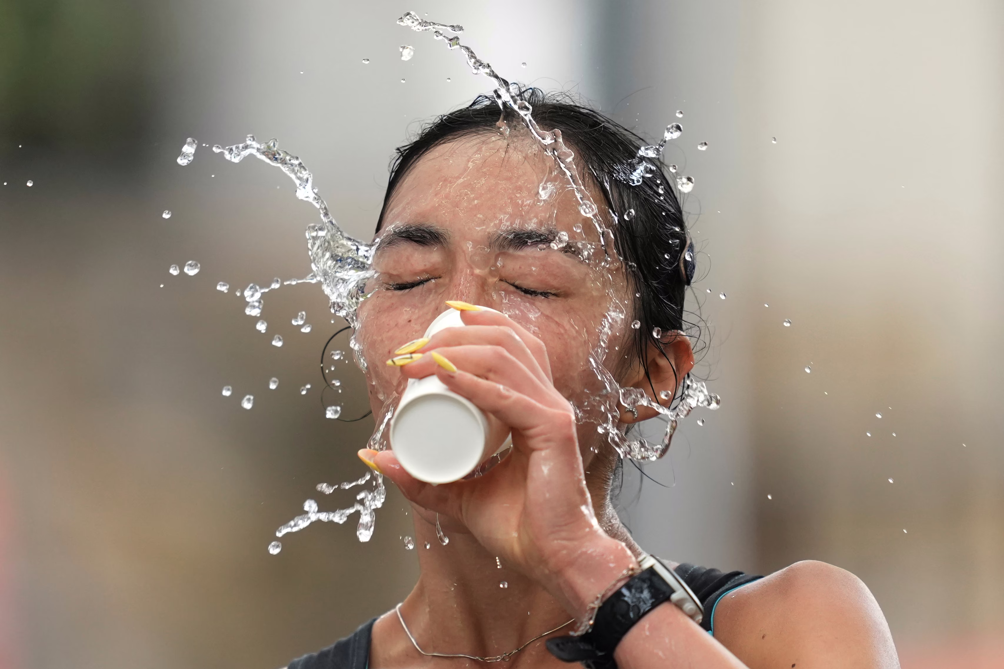 A competitor splashes a cup of water in their face during a marathon walk.