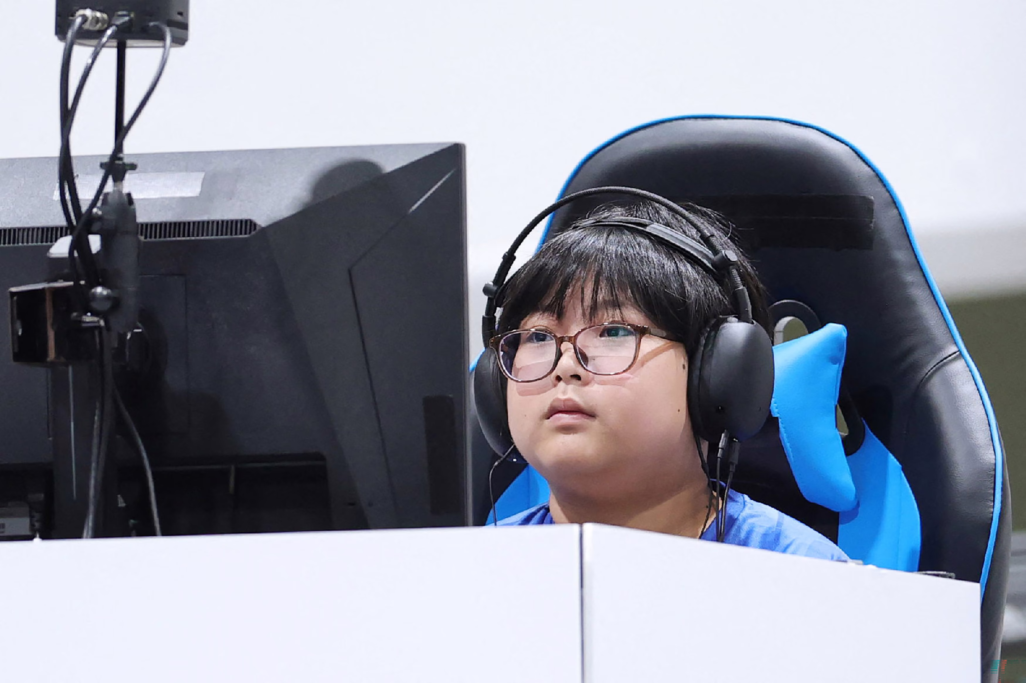 A boy wears headphones, sitting at a gaming station during a competition.