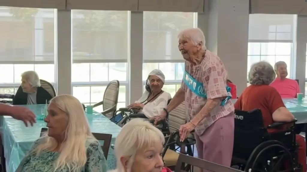 Blynda Vidock, a 105-year-old woman, standing with a walker and wearing a blue 