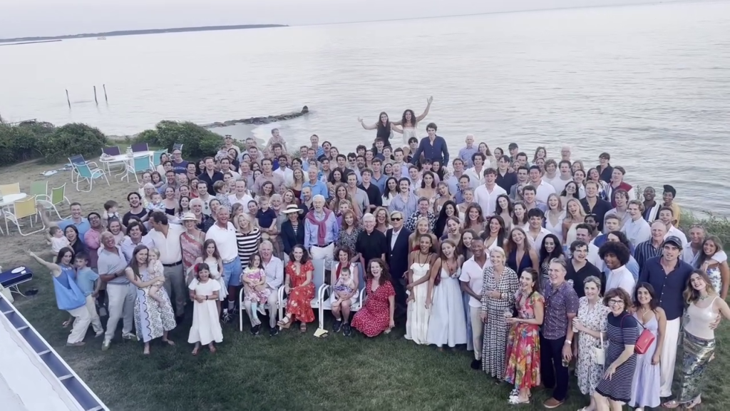 A large group of people, including John F. Kennedy and Jacqueline Kennedy, gather for a photo by the water.