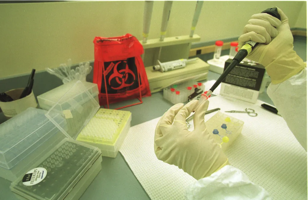 A scientist in yellow gloves handling DNA extractions in a lab.