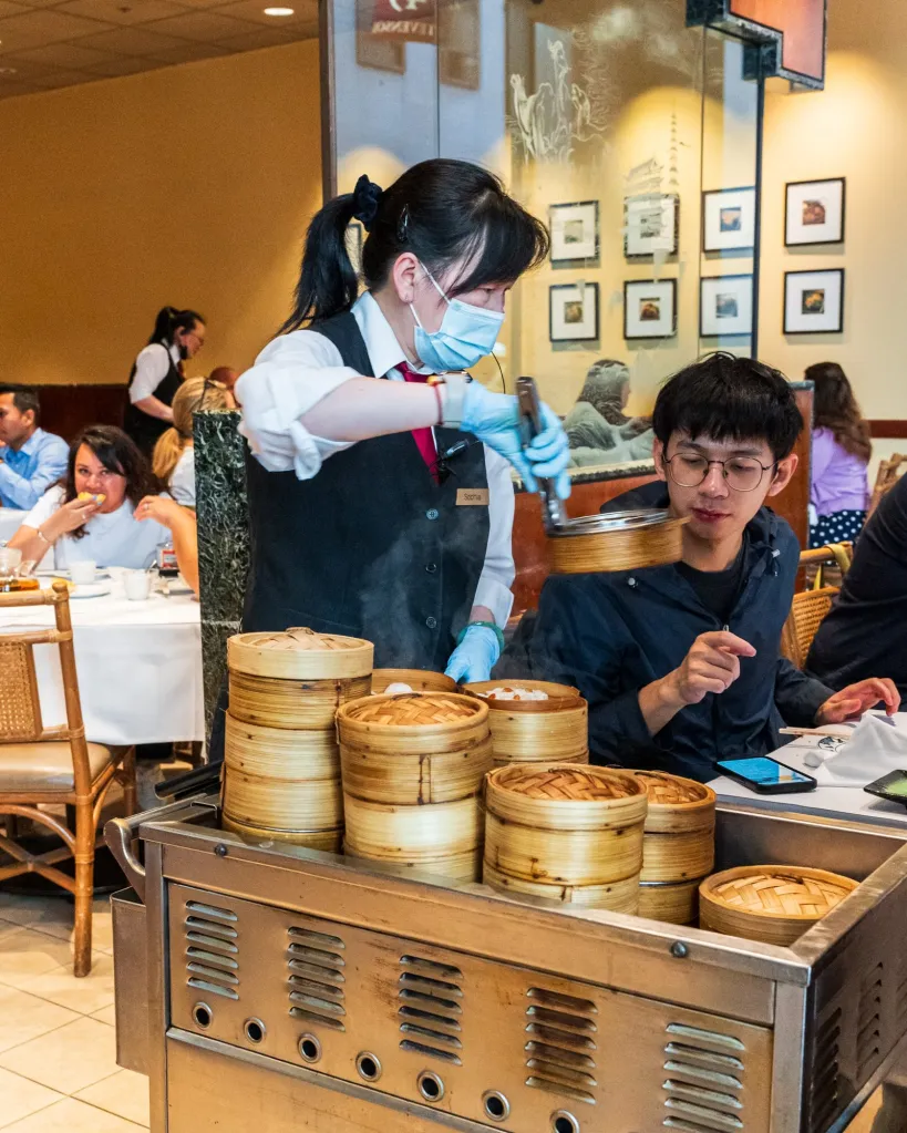 A server in a face mask and gloves serves a customer dim sum from a cart at Yank Sing restaurant.