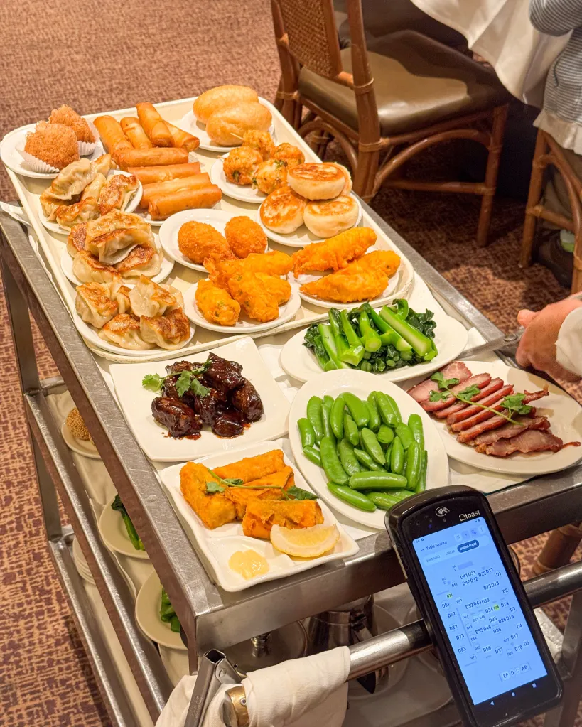 A dim sum cart loaded with various dishes, including dumplings, spring rolls, and roasted pork.