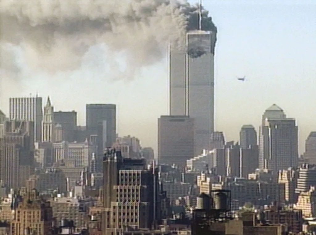 A hijacked plane approaching the South Tower of the World Trade Center in New York City with smoke billowing from the North Tower.