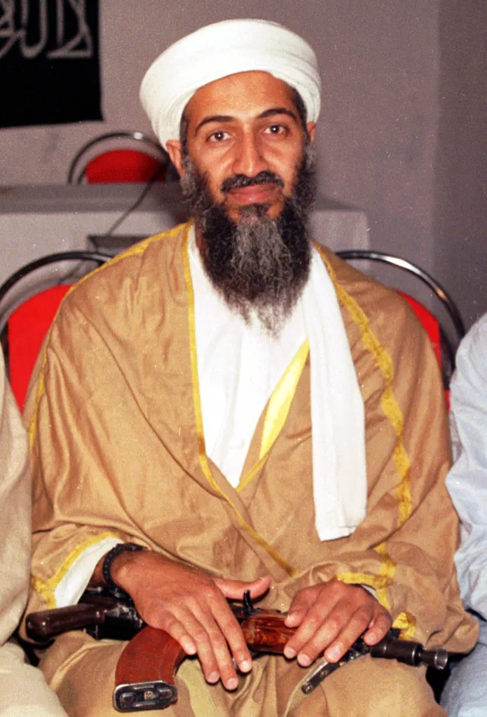 Osama bin Laden in traditional garb with a rifle on his lap.