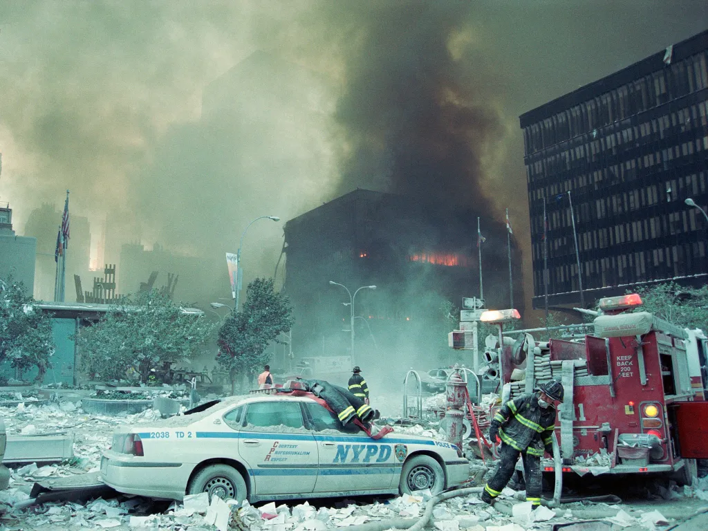 A New York City police car and a fire truck surrounded by debris and smoke following the 9/11 attacks.