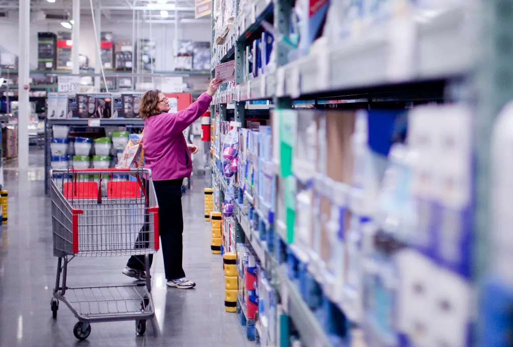 A woman shopping at a wholesale club, reaching for an item on a shelf.