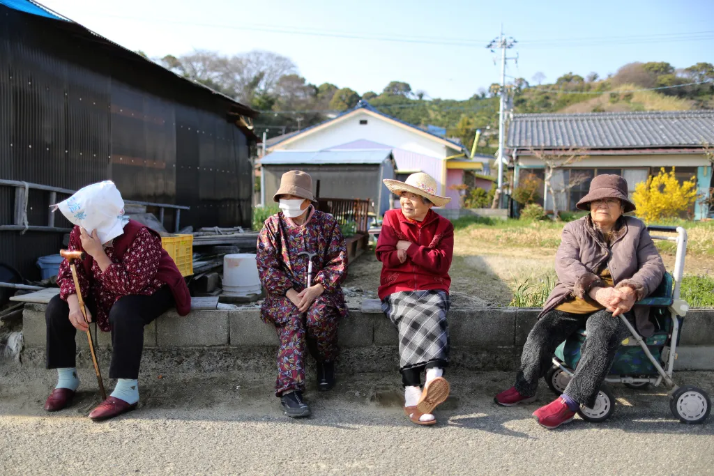 Four elderly Japanese women sit along a road on Gogo Island.