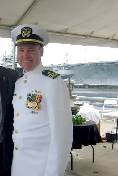 Christian Bradley Williams in a white naval uniform with a ship in the background.