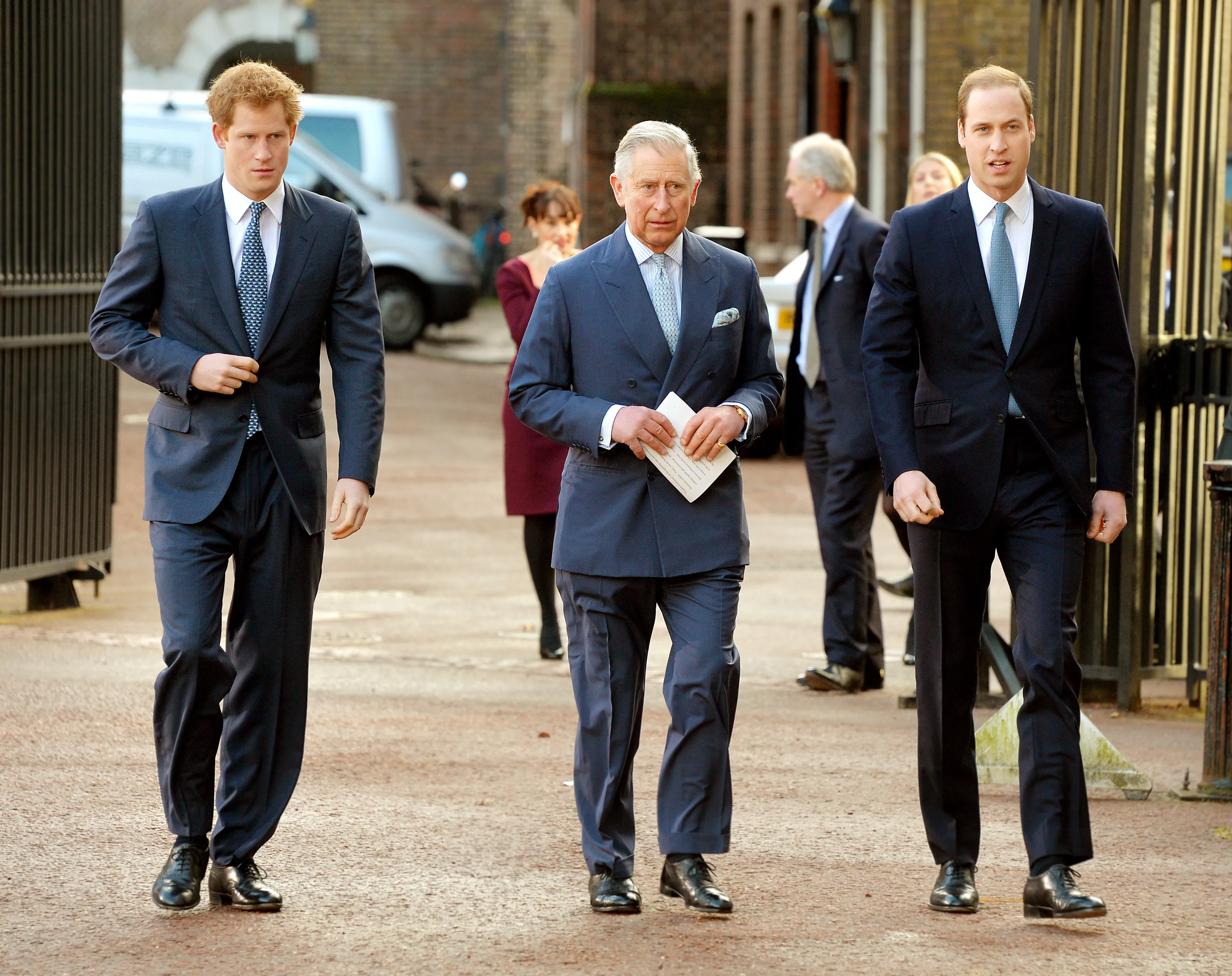 Prince Harry, Prince Charles, and Prince William walk in suits.